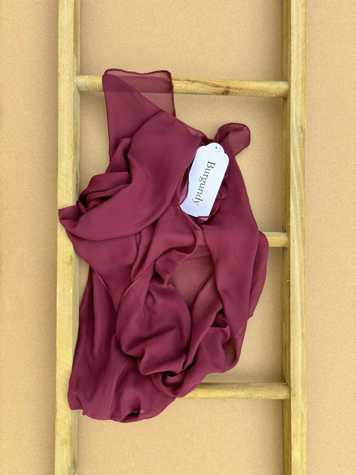 Chiffon Table Runner - Burgundy draped on a wooden ladder, available to hire for your wedding or event.
