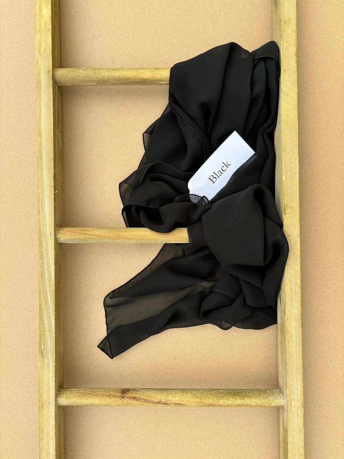 Chiffon Table Runner - Black loosely draped on a wooden ladder, available to hire for your wedding or event.