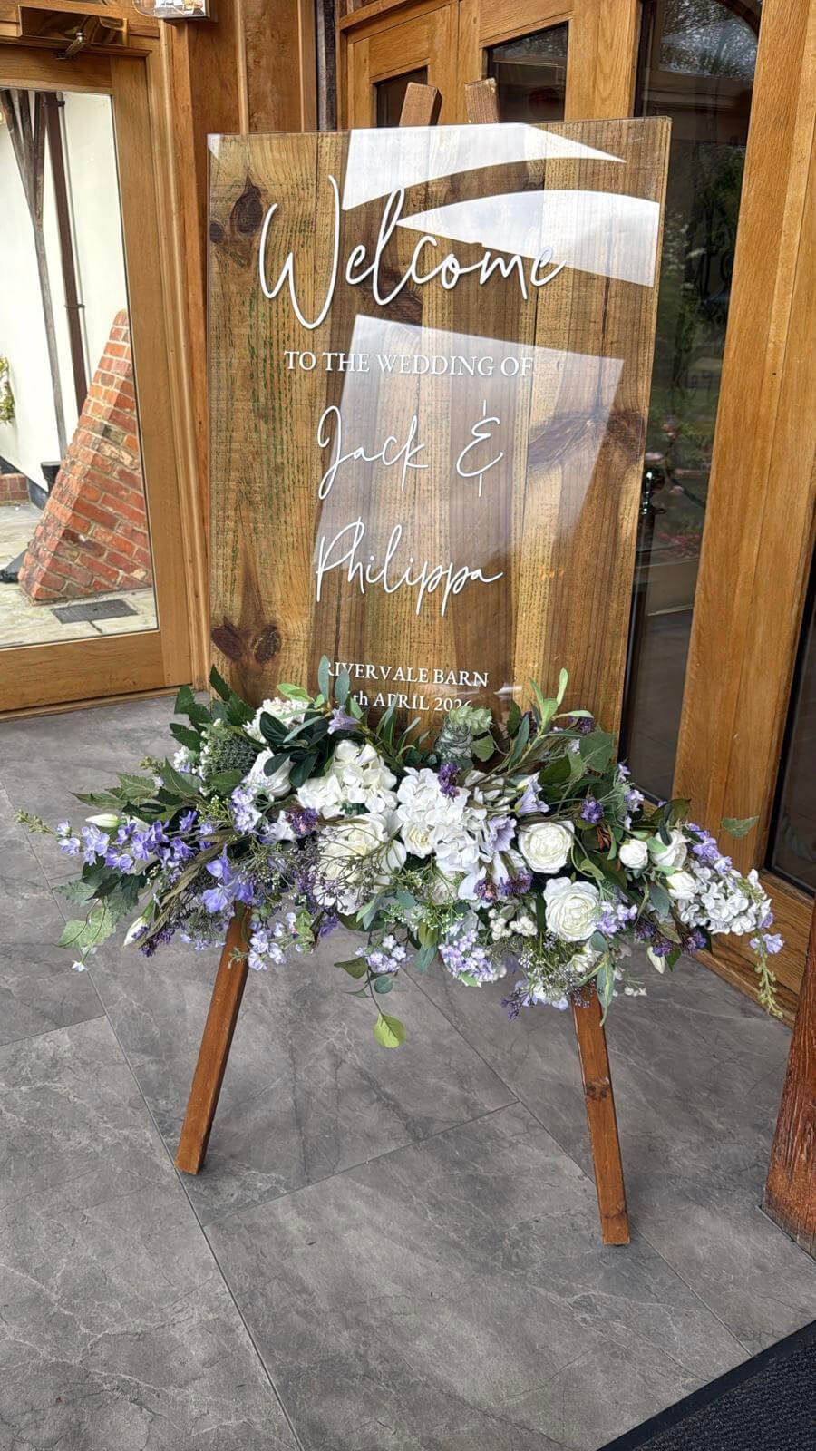 Faux Florals - Faux Floral accent for sign with white and purple flowers and greenery on a wooden easel, available to hire for your wedding or event.