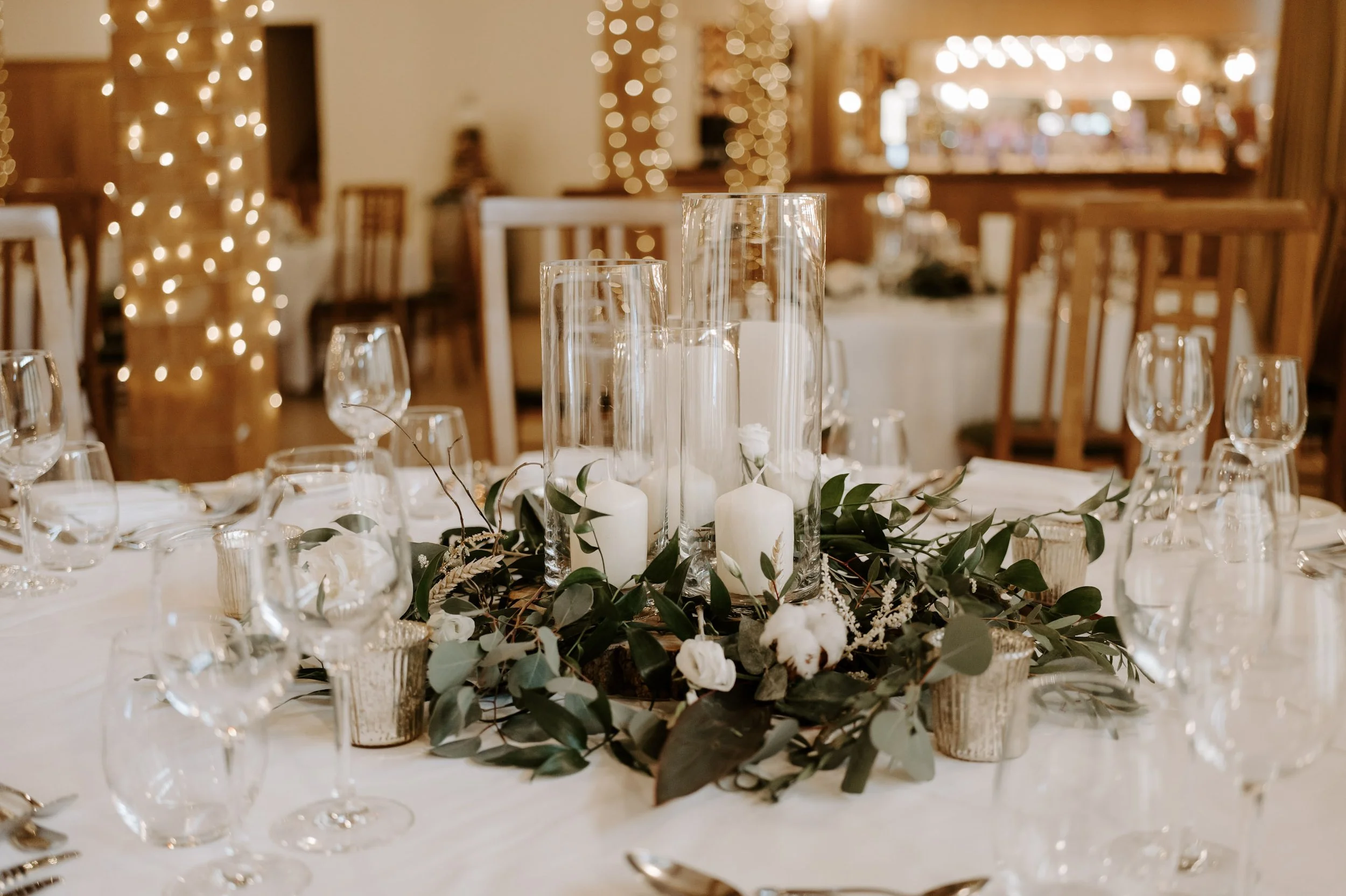 Faux Florals - Faux Flower wreath to fit 3 cylinder vases arranged with greenery and white flowers around three glass cylinder vases with white candles, available to hire for your wedding or event.