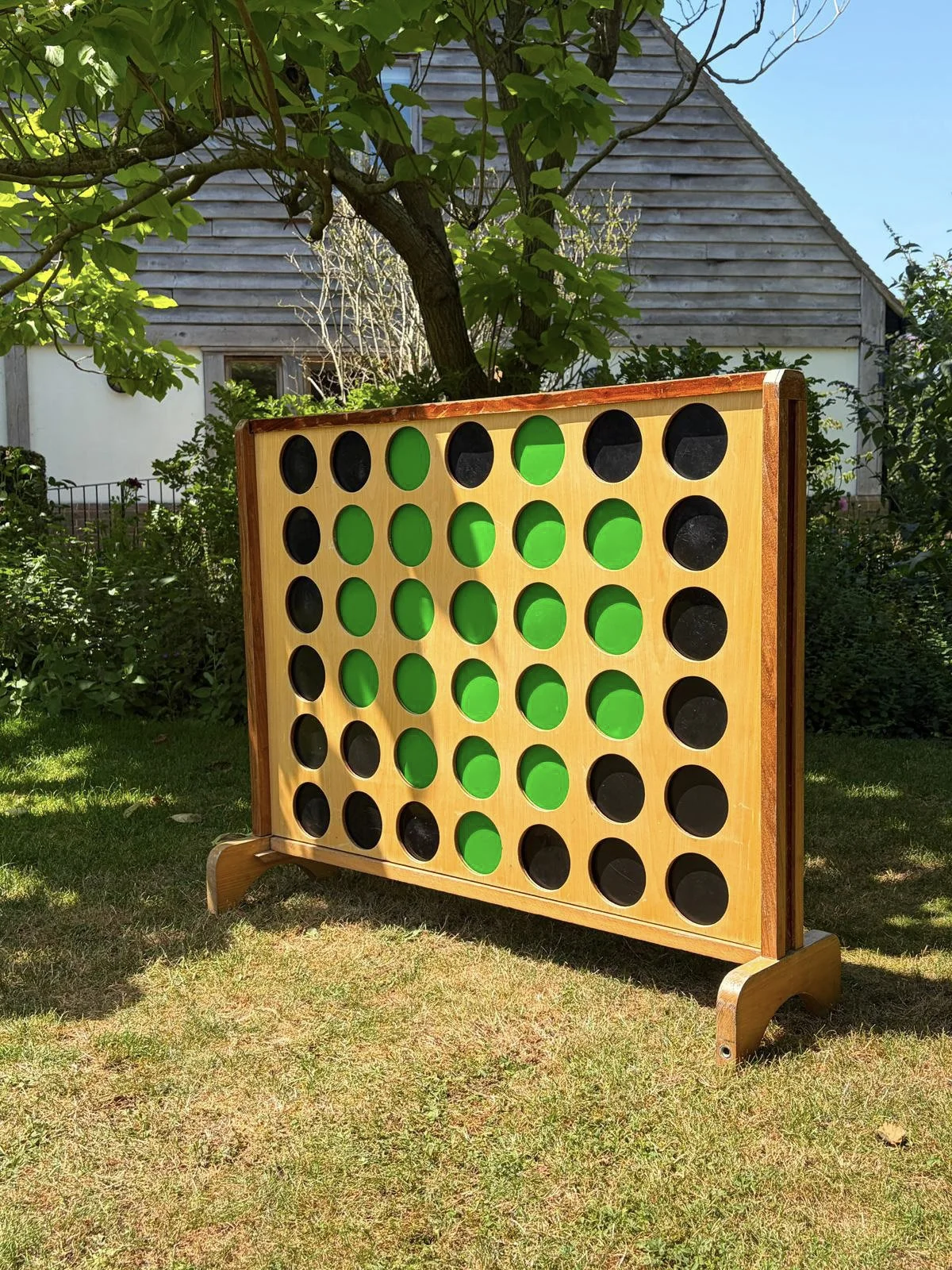 Giant Connect 4 - Wooden game set outdoors with green and black discs, available to hire for your wedding or event.