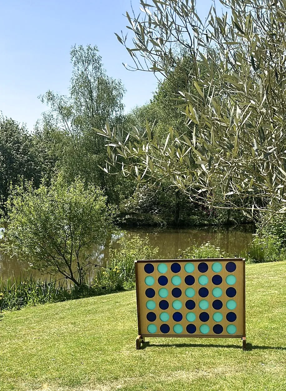 Giant Connect 4 - Wooden game set on grass by a pond, available to hire for your wedding or event.