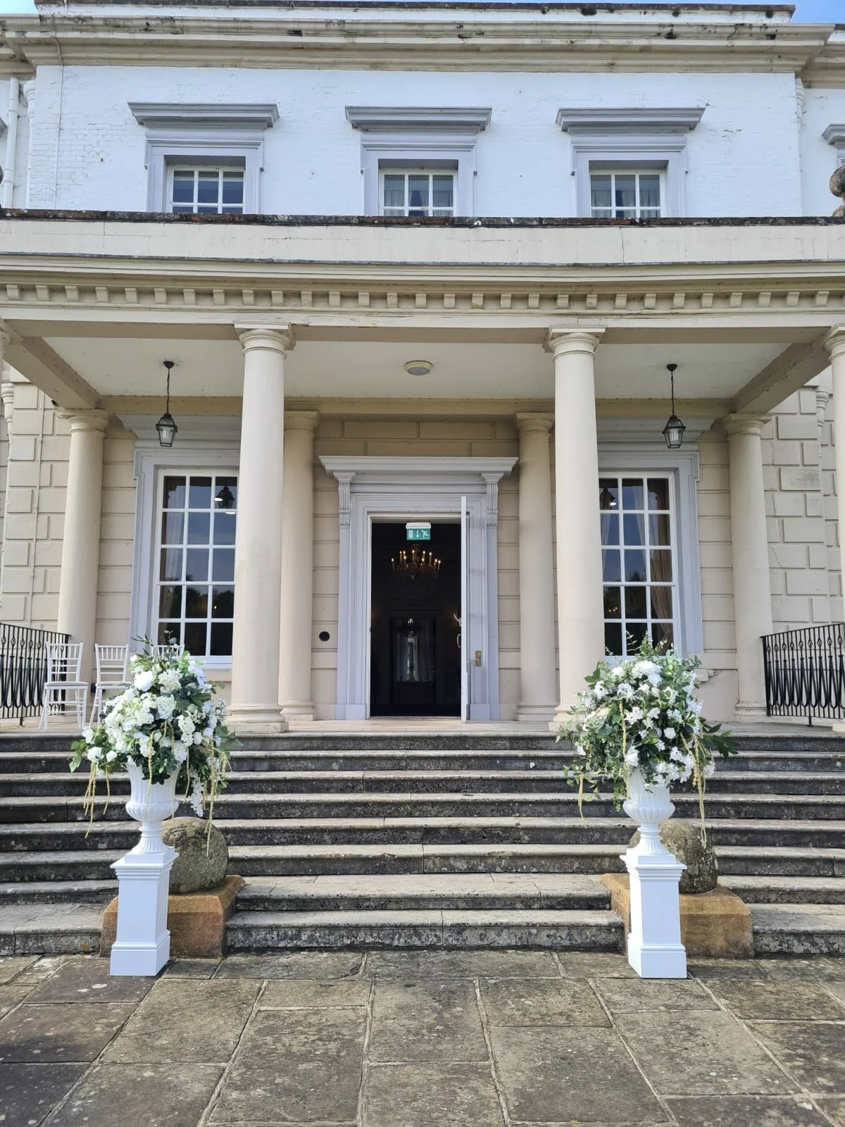White Plinth - Large 30x30x120cm topped with white floral arrangements on stone steps outside a grand building, available to hire for your wedding or event.