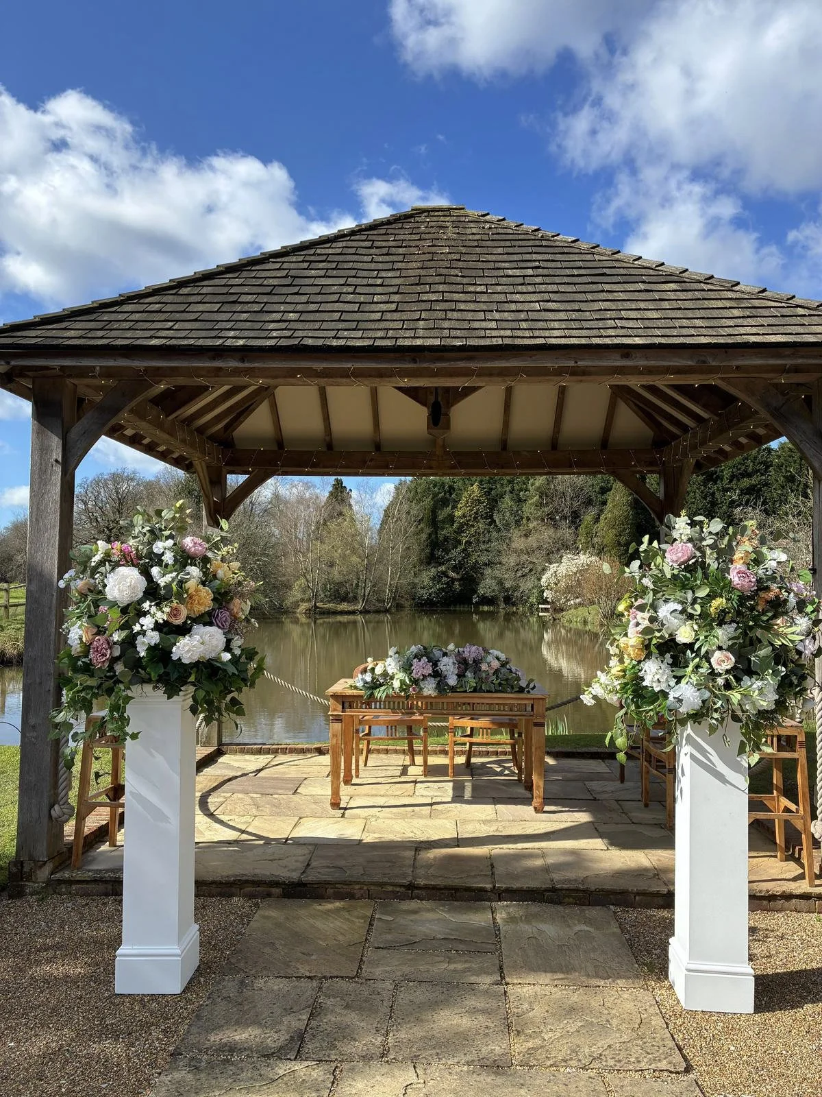 White Plinth - Large 30x30x120cm with floral arrangements under a wooden gazebo by a lake, available to hire for your wedding or event.