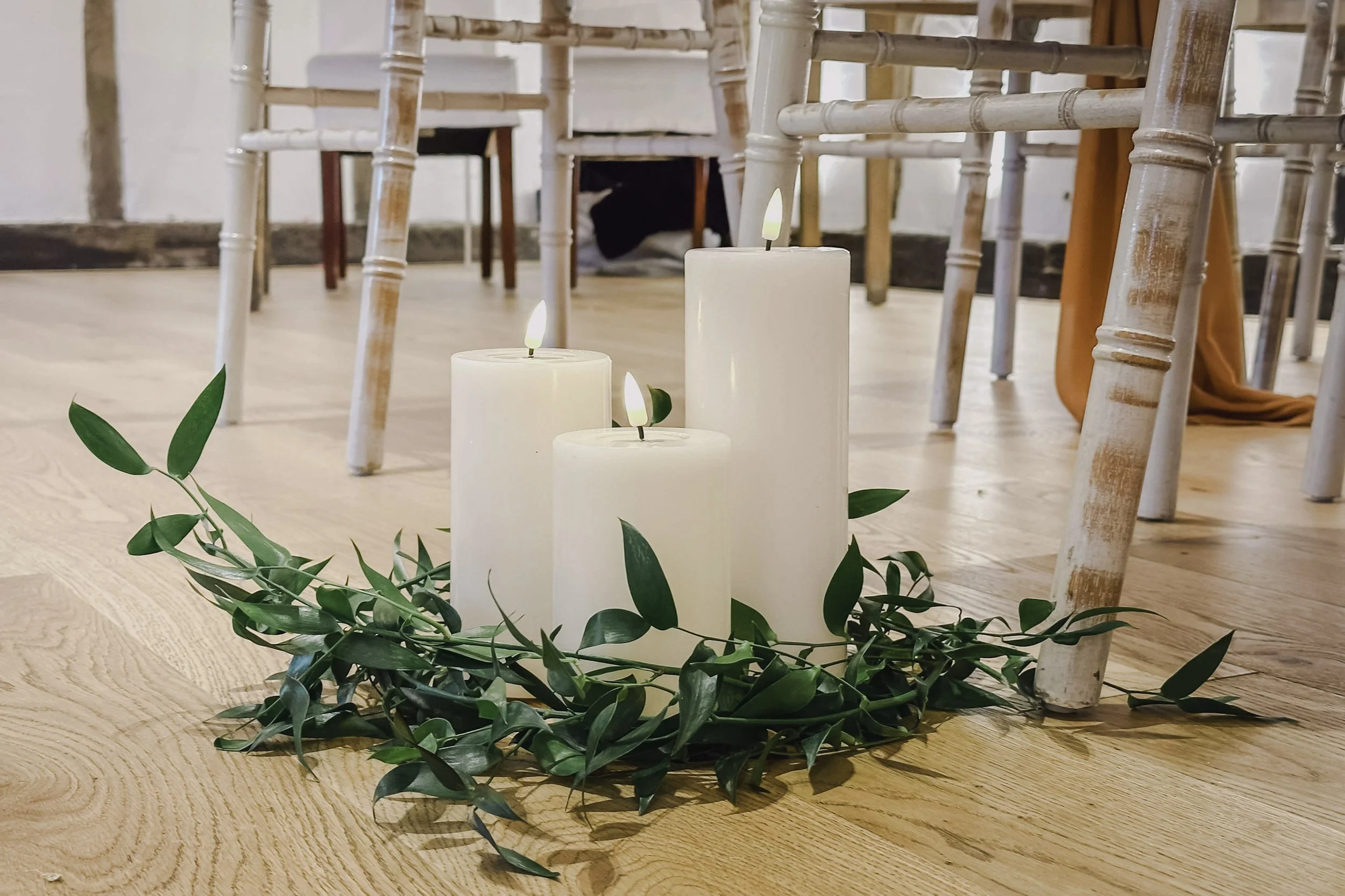 Deluxe LED Candle - Ivory Chapel Small (7.5cmW x 15cmH) arranged with greenery on wooden floor, available to hire for your wedding or event.