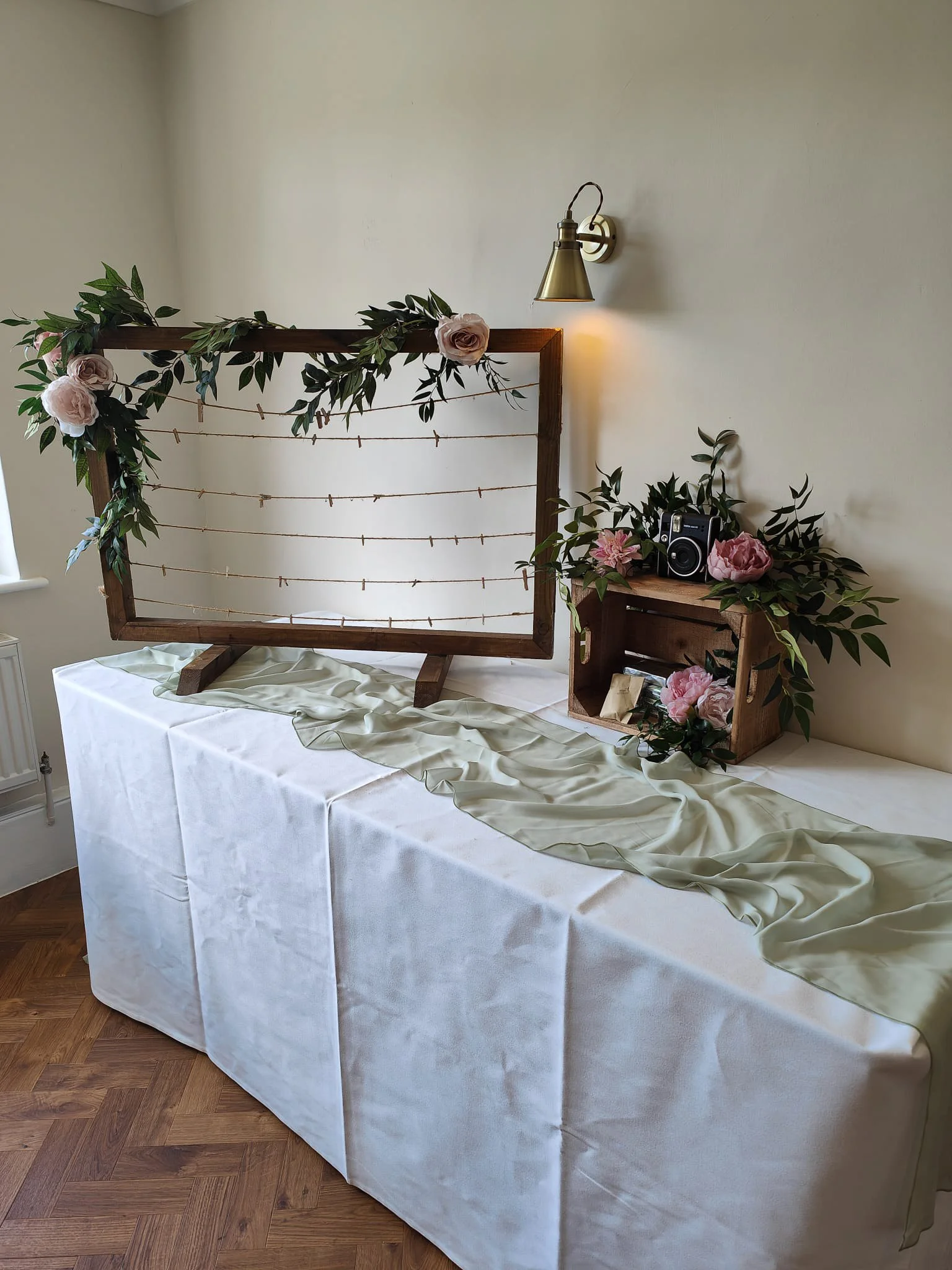 Hanging wedding display frame styled with Polaroid photos, greenery and a table display