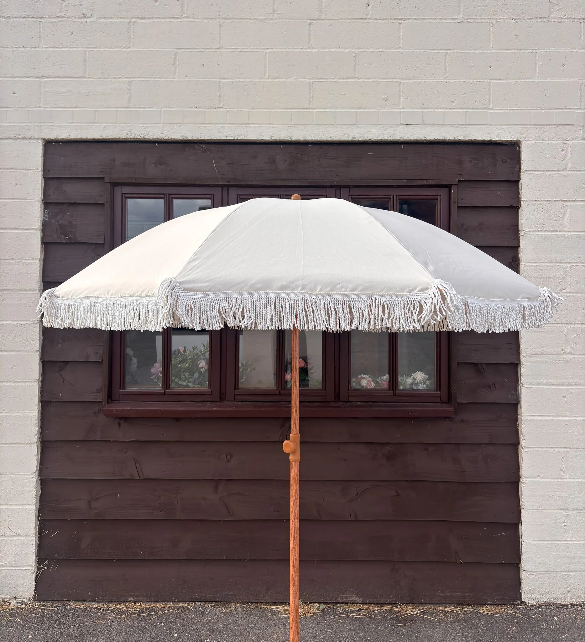 Beige fabric wedding parasol with decorative fringe and wooden pole for outdoor event hire