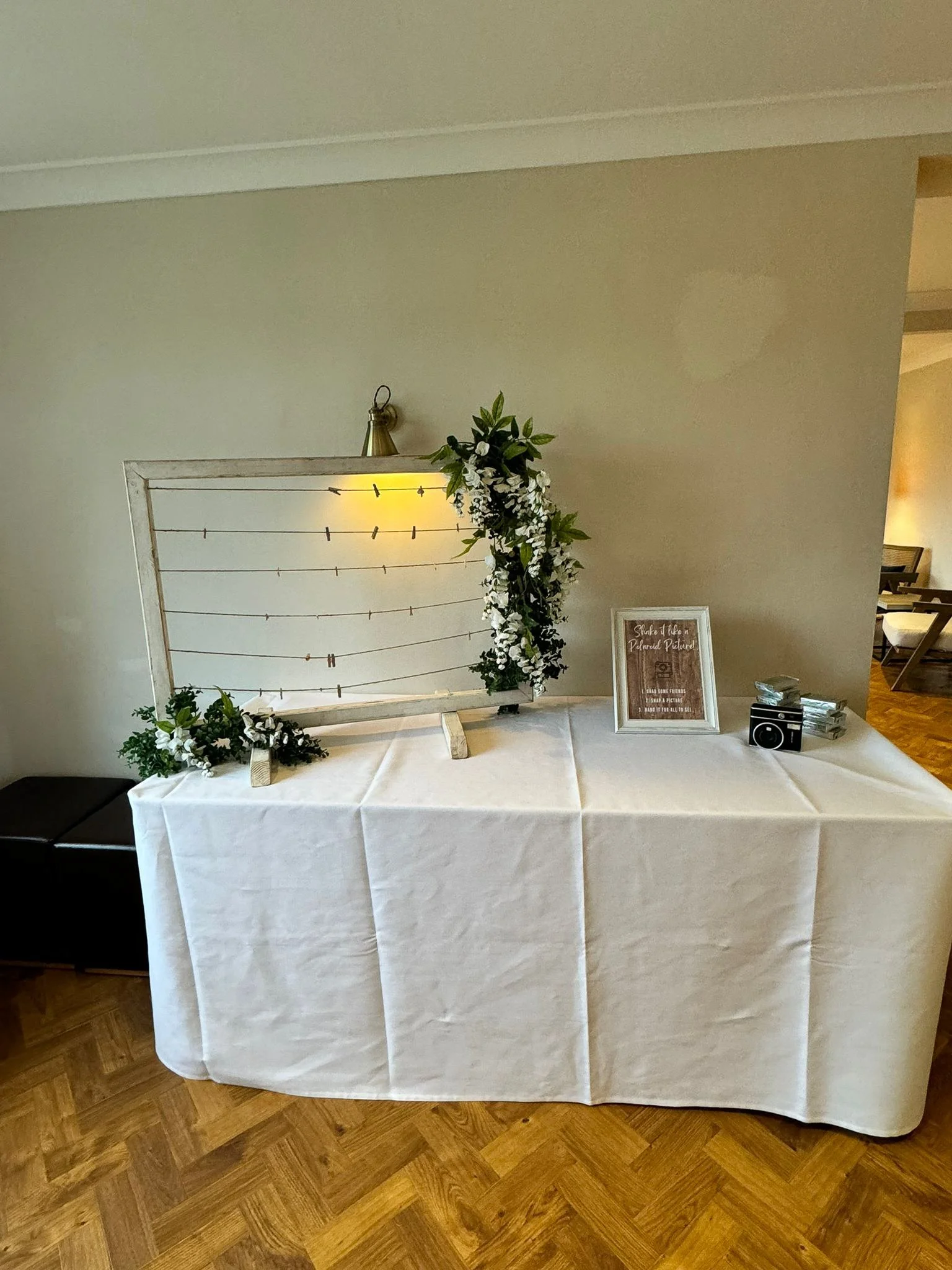Hanging wedding display frame styled with Polaroid photos, greenery and a table display