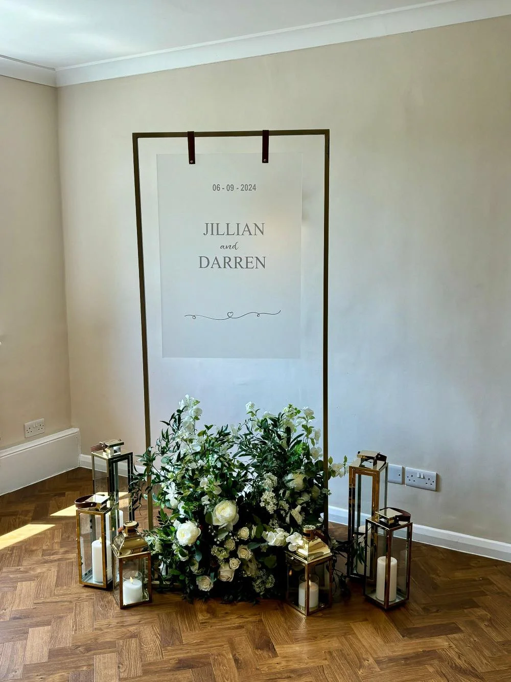 Black hanging wedding welcome sign frame decorated with white flowers and greenery