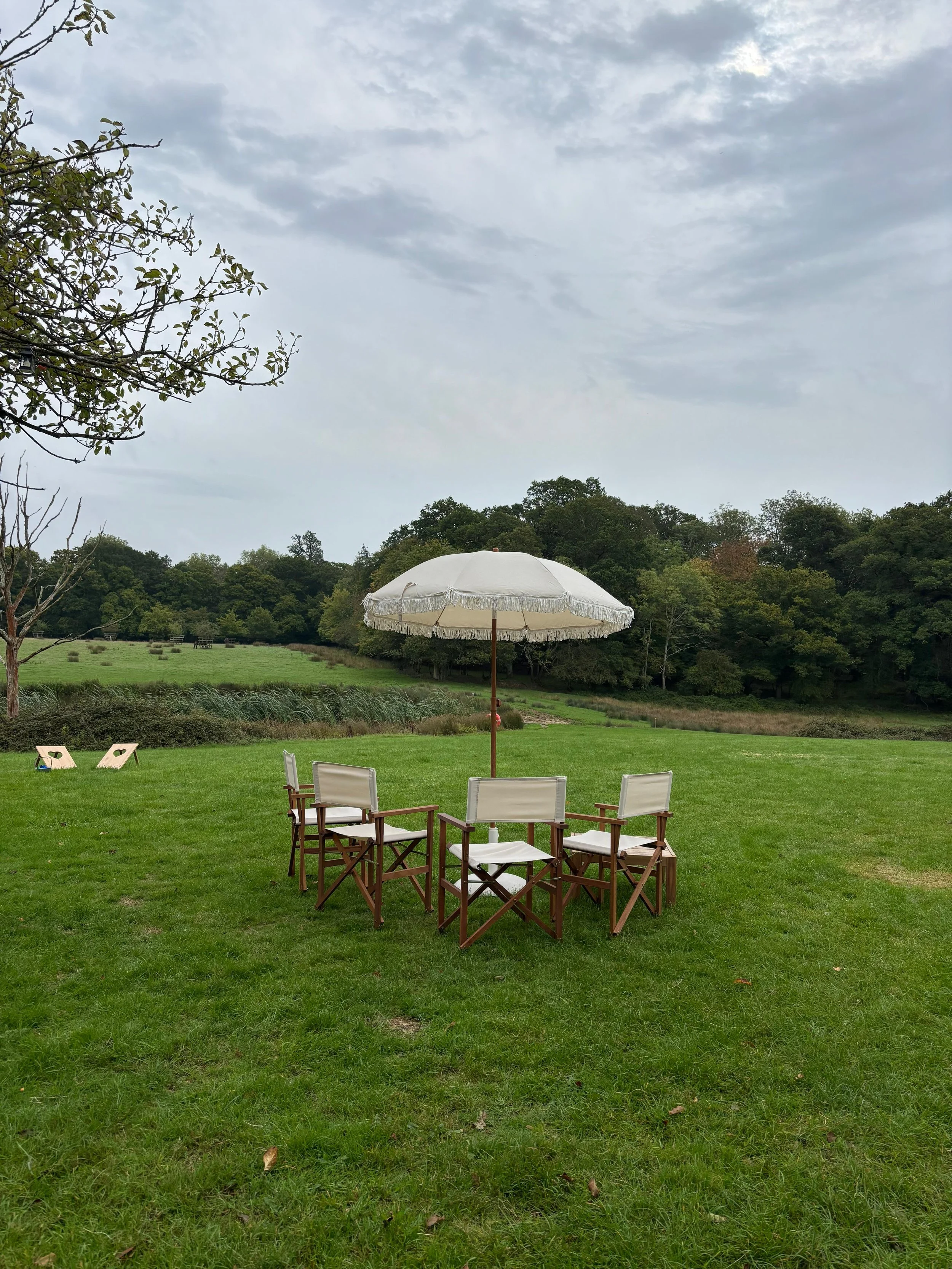 Beige fabric wedding parasol with decorative fringe and wooden pole for outdoor event hire