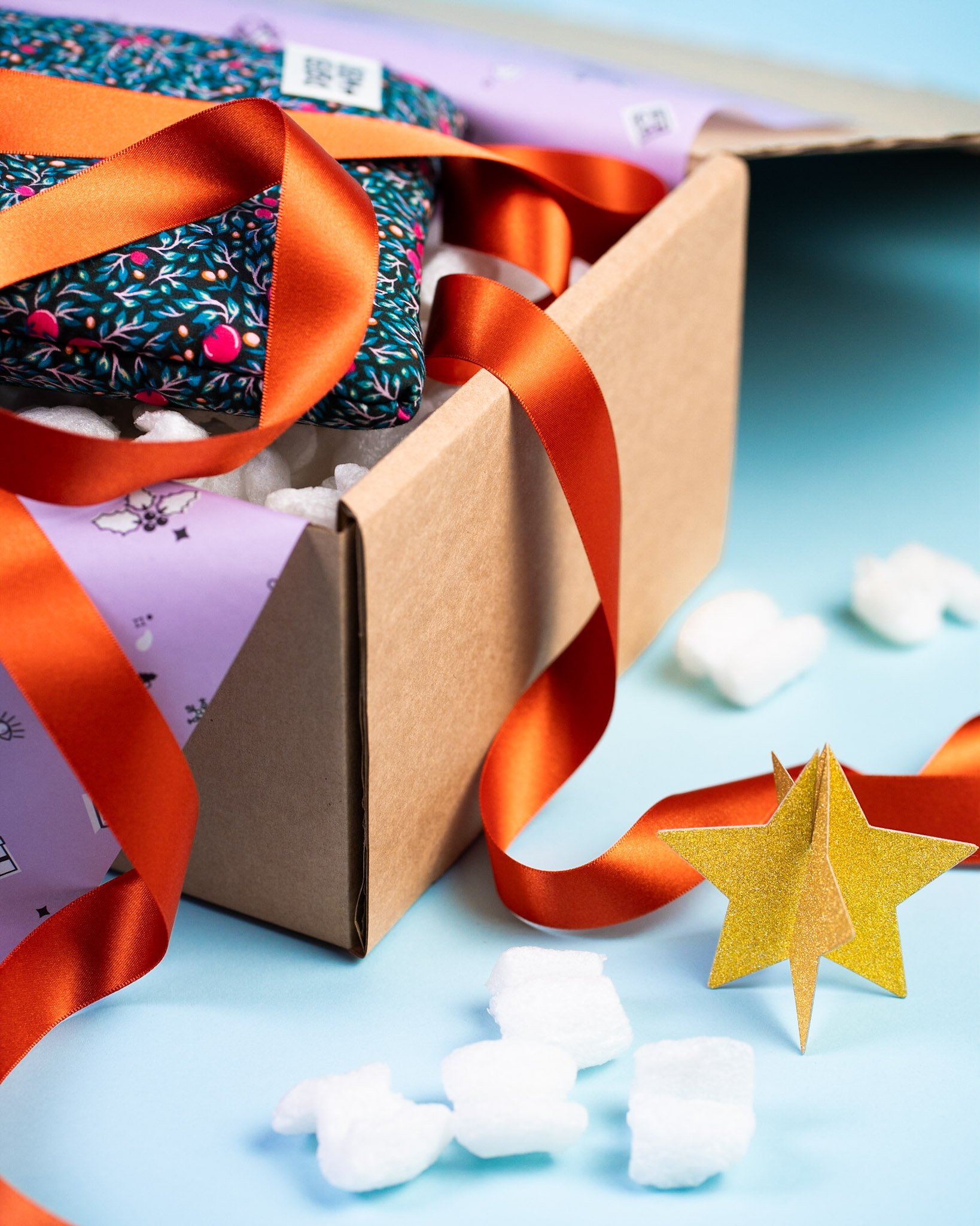 Photo of a Christmas book sleeve wrapped in gift wrap packaging. There is a loose ribbon draped over the box ready to be tied and a gold Christmas star decoration