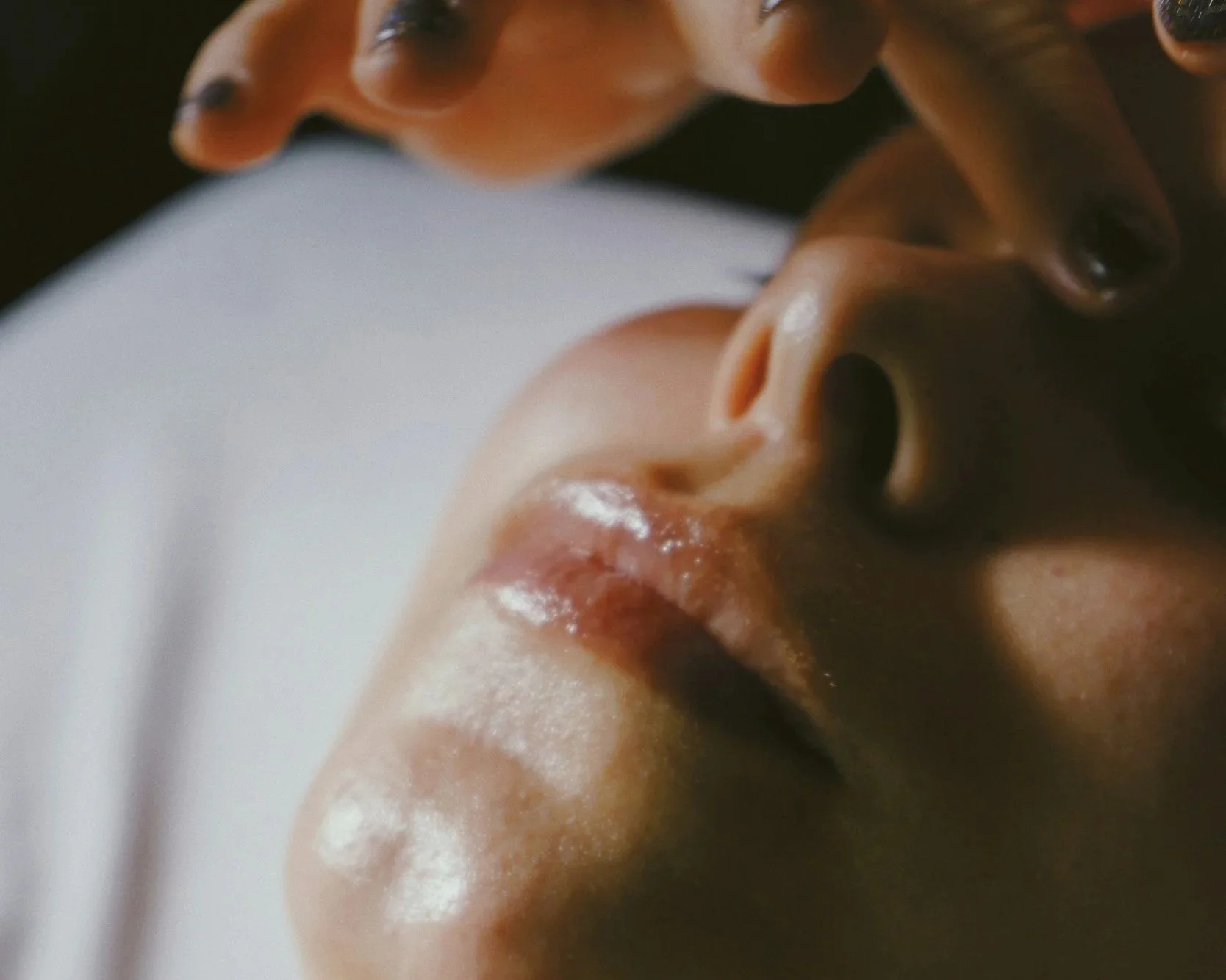 close up of woman receiving facial with her eyes closed and the esthetician's fingers touching her forehead.