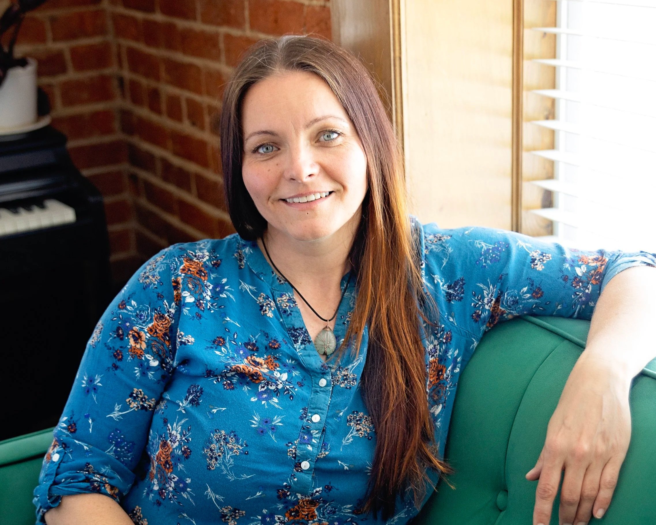 Photo of Amanda Snow, LMT, smiling, in blue shirt sitting on a green sofa.