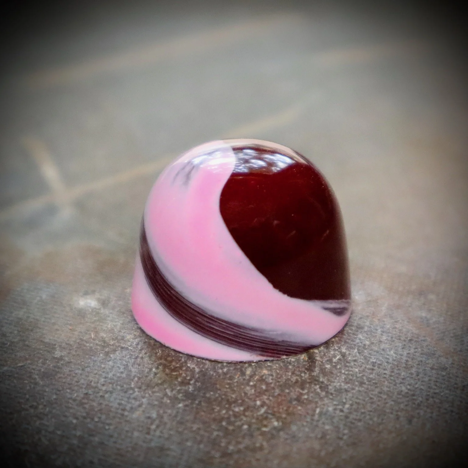 Close-up of a pink, white, and dark red marble on a concrete surface.
