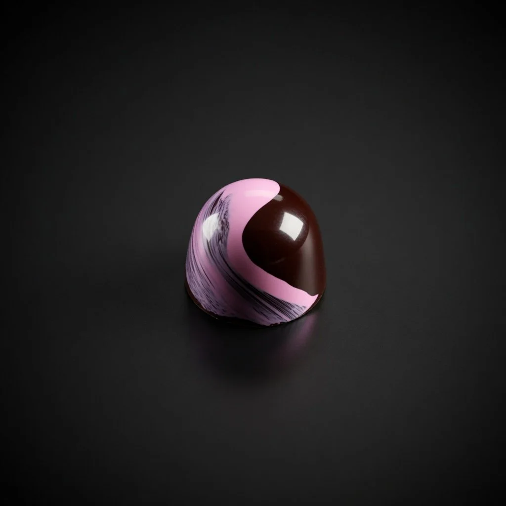 A glossy pink, purple, and dark chocolate bonbon with bold marbled swirls, sharply in focus and well lit, resting on a solid matte black background with realistic contact shadow.