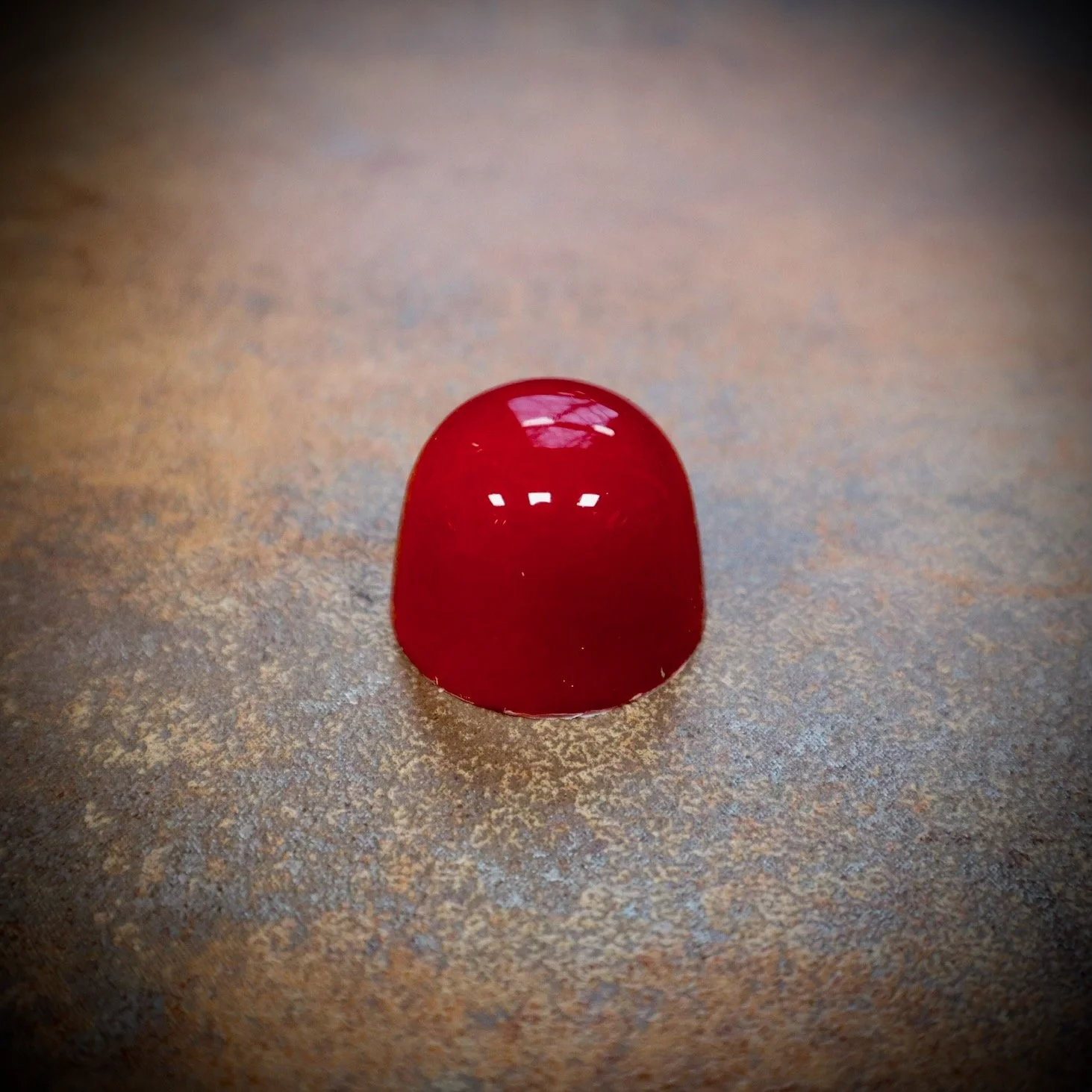 A single glossy red chocolate bonbon on a textured surface.