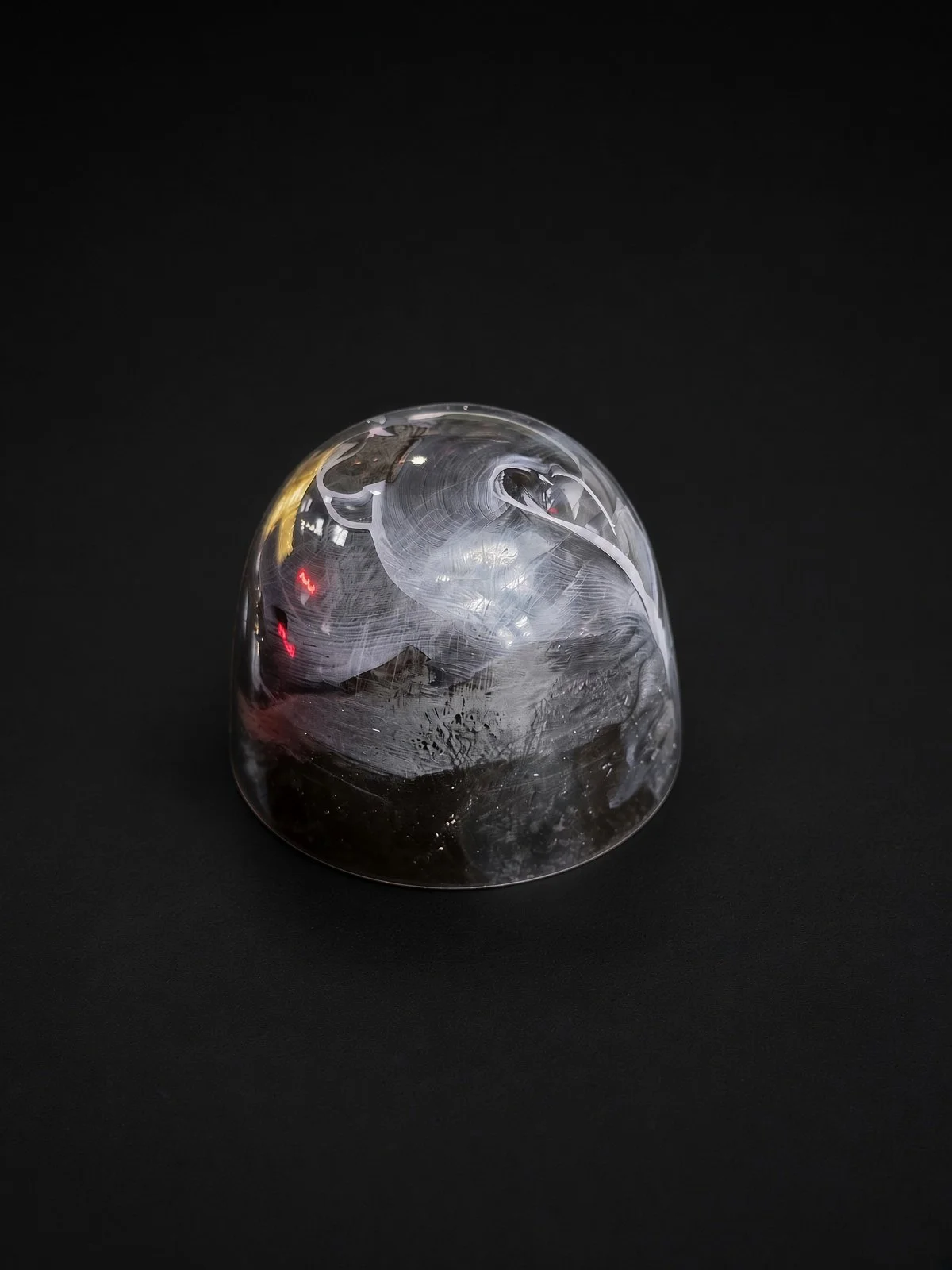 A glossy chocolate bonbon with a clear, smoky shell showing white brushed swirls over dark chocolate, sharply in focus and well lit, resting on a solid matte black background.