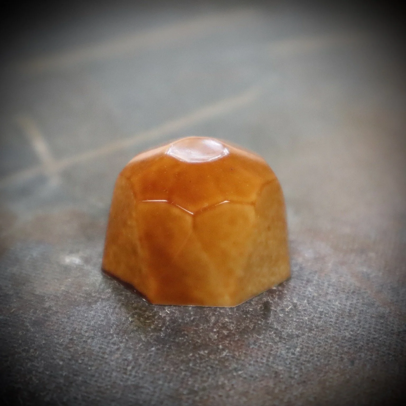 Close-up of a small, brown, honeycomb-shaped object with a shiny surface on a metallic surface.