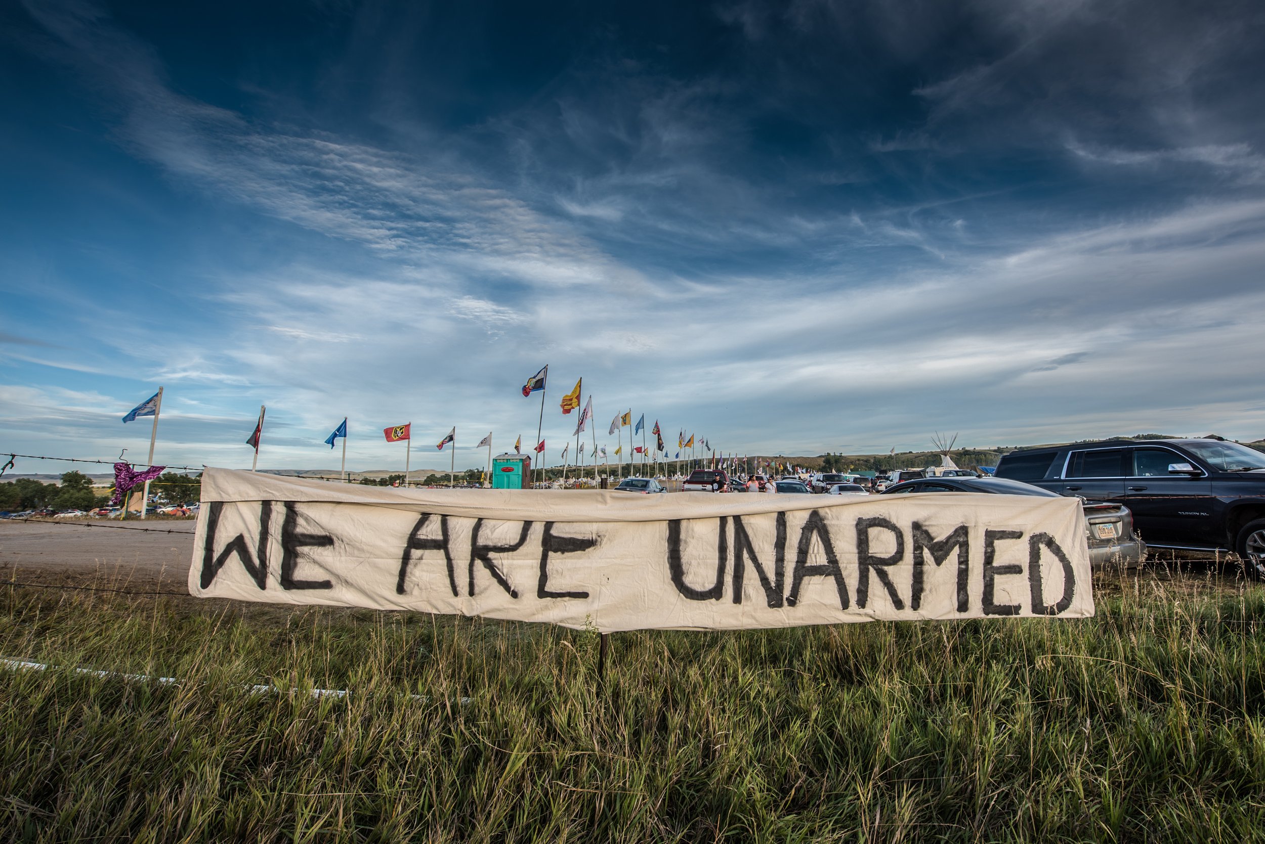  This large banner hung at the edge of the Oceti Sakowin encampment at Standing Rock, adjacent to ND Highway 1806. The impetus for this banner was over concerns that police were concerned that weapons existed within the encampment. 
