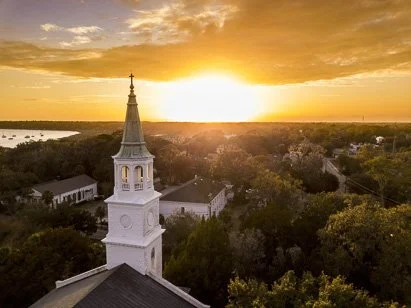 Aerial view of a historic white church steeple and community buildings at sunset, representing campus safety and fire-extinguisher-inspection-denver-private-institutions. compliance services for local religious organizations.
