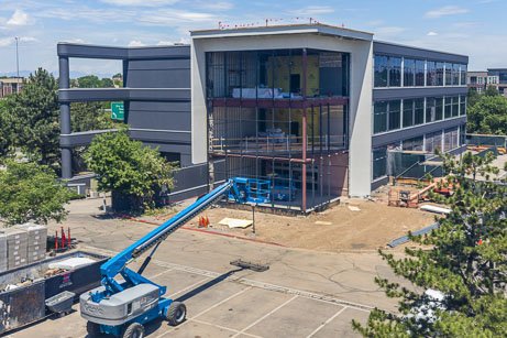 An active commercial construction site featuring a multi-story building frame and a blue boom lift, highlighting job site safety compliance and fire extinguisher inspection Denver construction services.