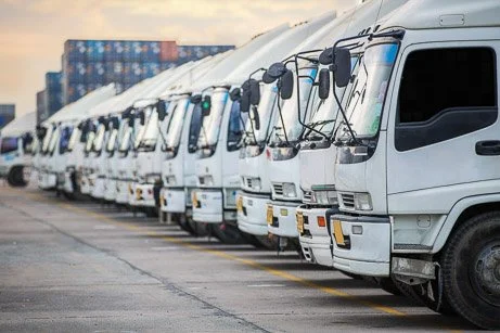A long line of white commercial delivery trucks parked in a shipping depot, highlighting DOT compliance and mobile fire extinguisher inspection automotive Denver services.