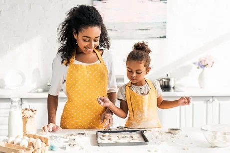 A mother and young daughter wearing yellow aprons baking cookies together in a bright kitchen, emphasizing home kitchen fire safety and residential fire extinguisher services.