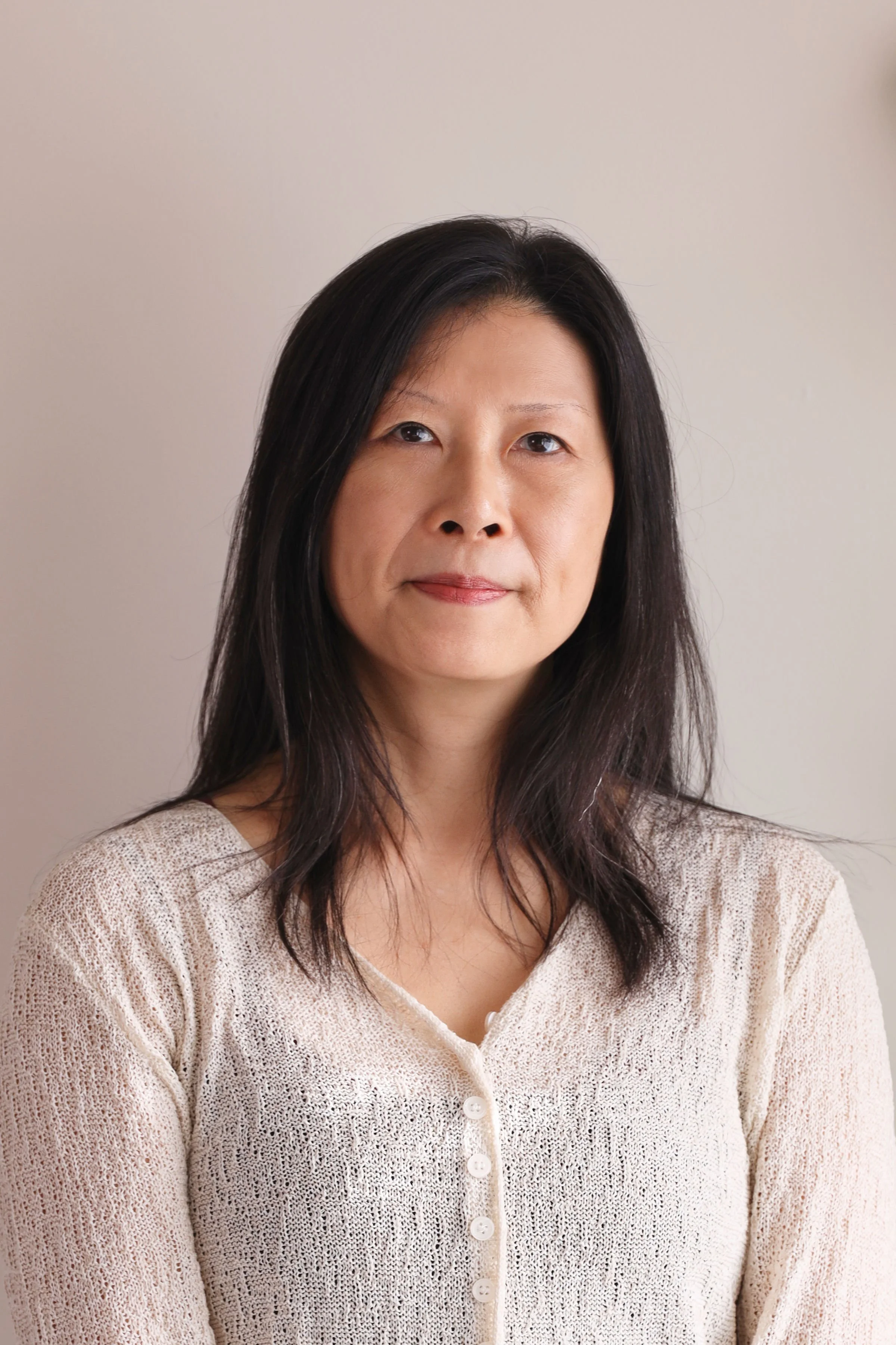 Portrait of a woman with shoulder-length dark hair wearing a cream-colored buttoned cardigan against a neutral background.
