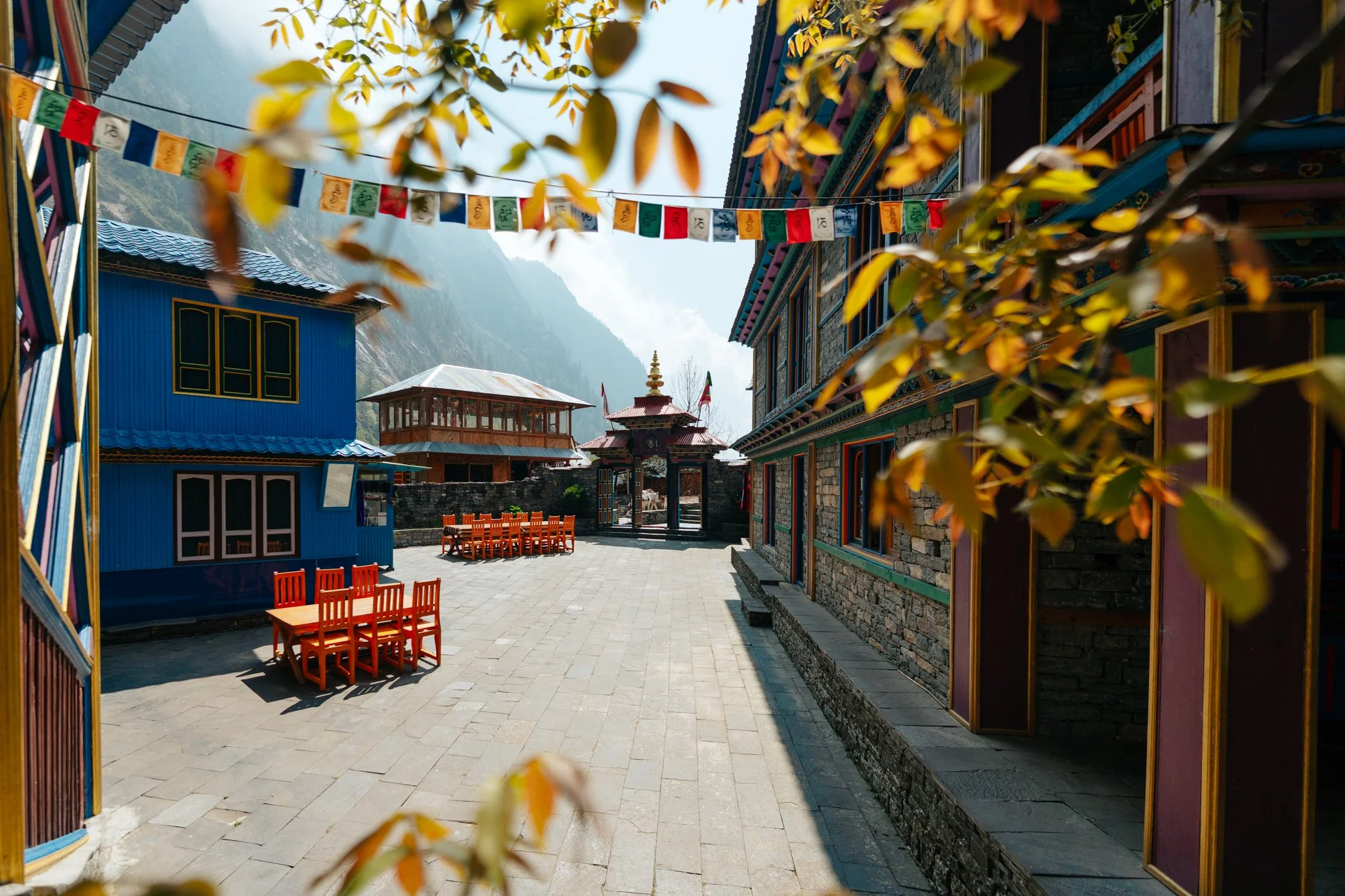 Namrung village square with Tibetan prayer flags, orange tables outside a monastery gate, and a yak on the Manaslu Circuit Trek