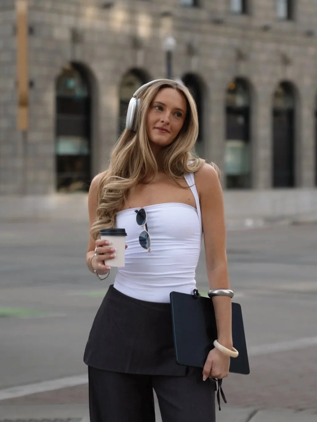 Karlie Place walking through downtown Salt Lake City wearing headphones and holding a coffee and laptop
