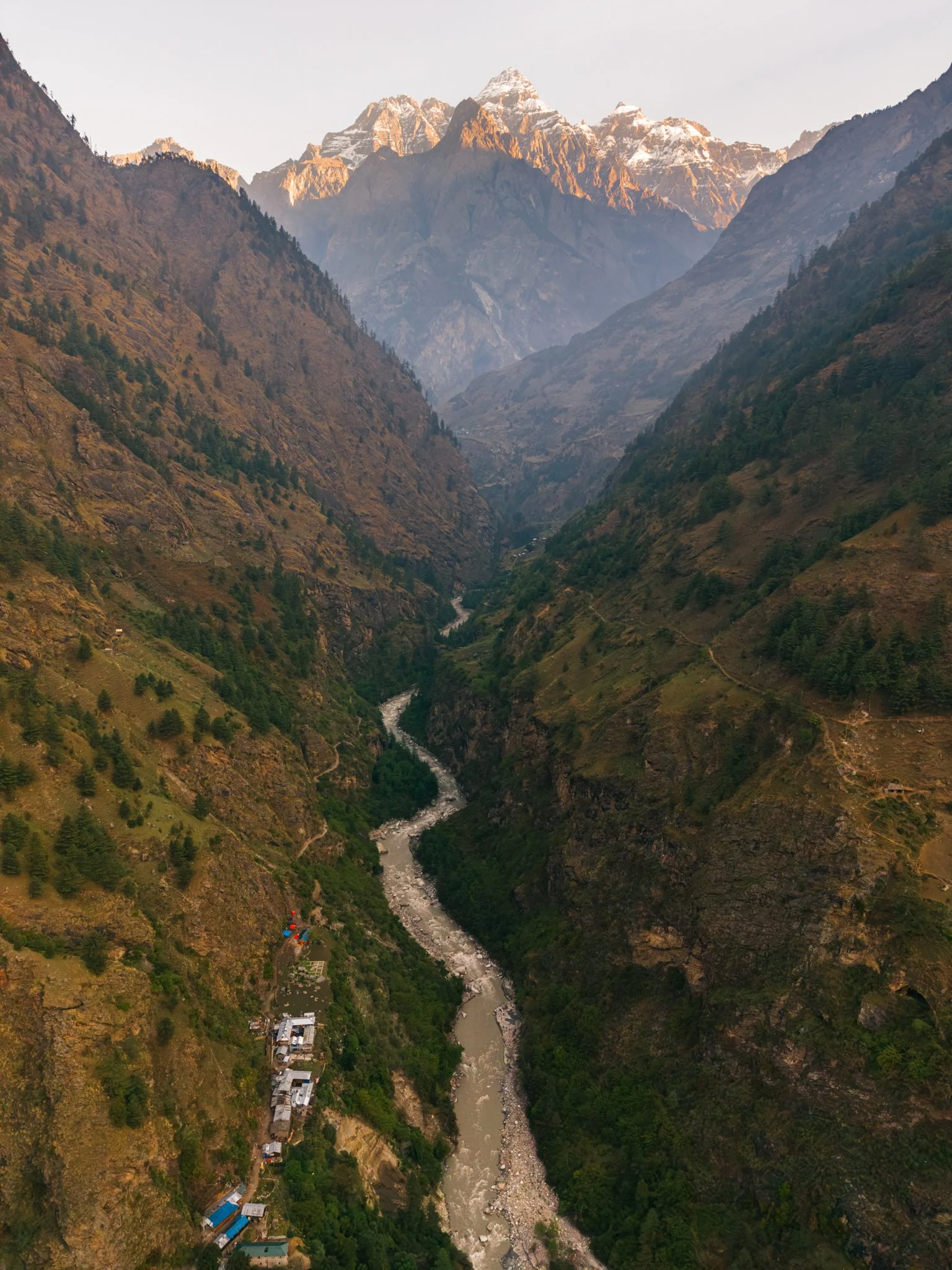 Drone aerial view over Deng village looking up the Budhi Gandaki valley toward distant Himalayan peaks on the Manaslu Circuit Trek