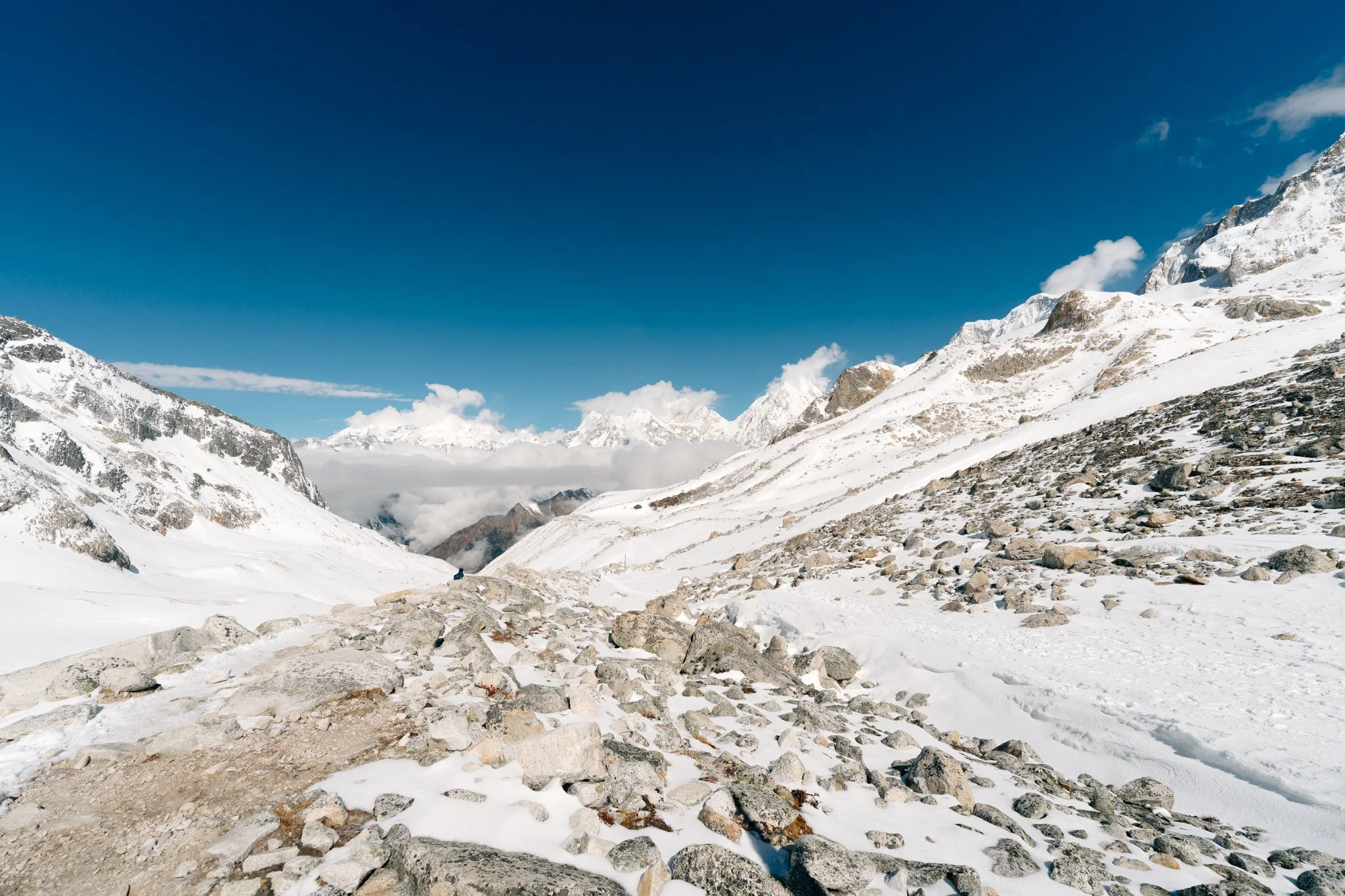 Solo female trekker celebrating with a mid-air jump at Larkya La Pass sign at 5,106 meters elevation with prayer flags tangled overhead on the Manaslu Circuit Trek