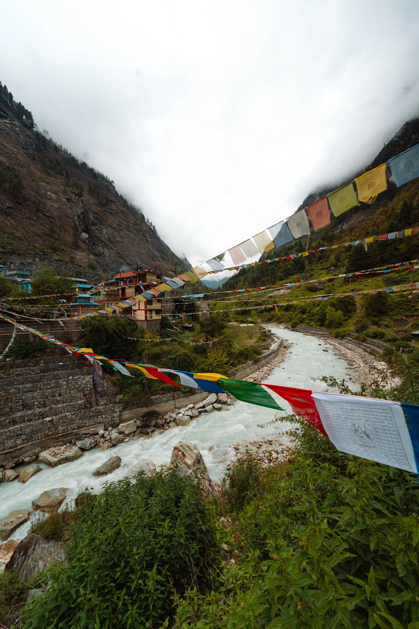 Tilije and Dharapani villages along the milky-turquoise Marsyangdi river with layered Tibetan prayer flags overhead at the end of the Manaslu Circuit Trek