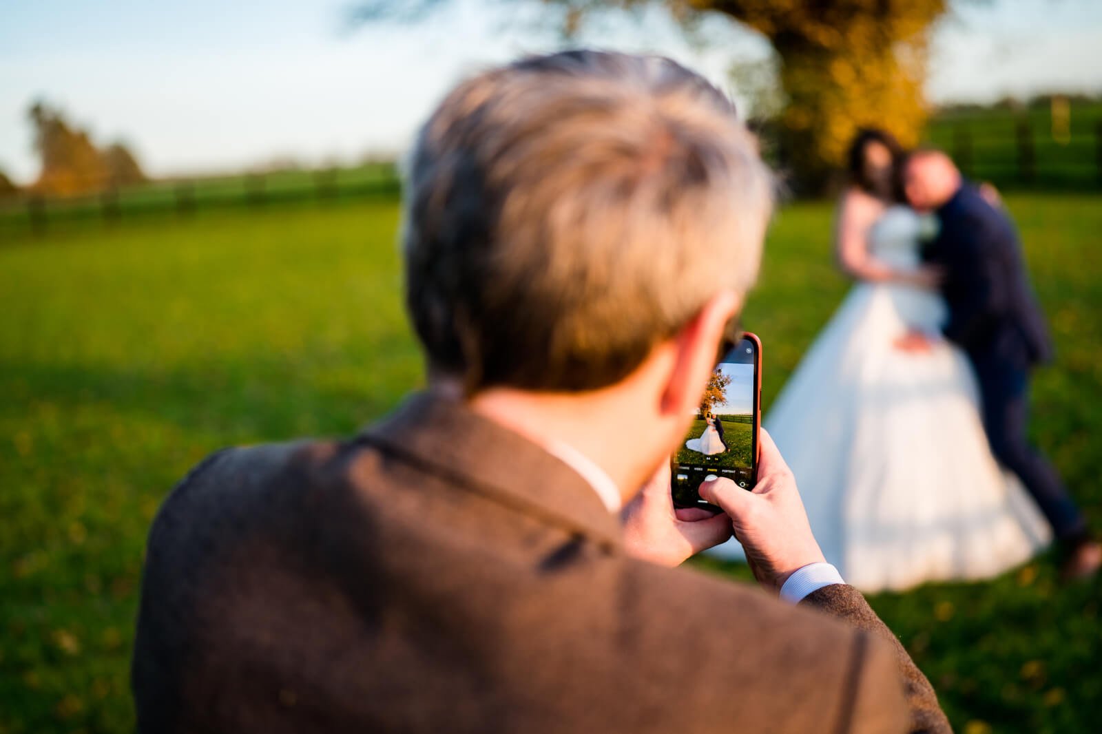 guest takes photo of bride and groom at sunset at barford park barn