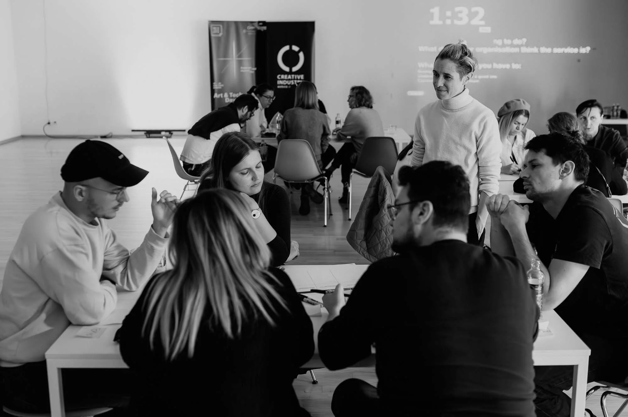 A person stands over a group sitting discussing a topic at a table