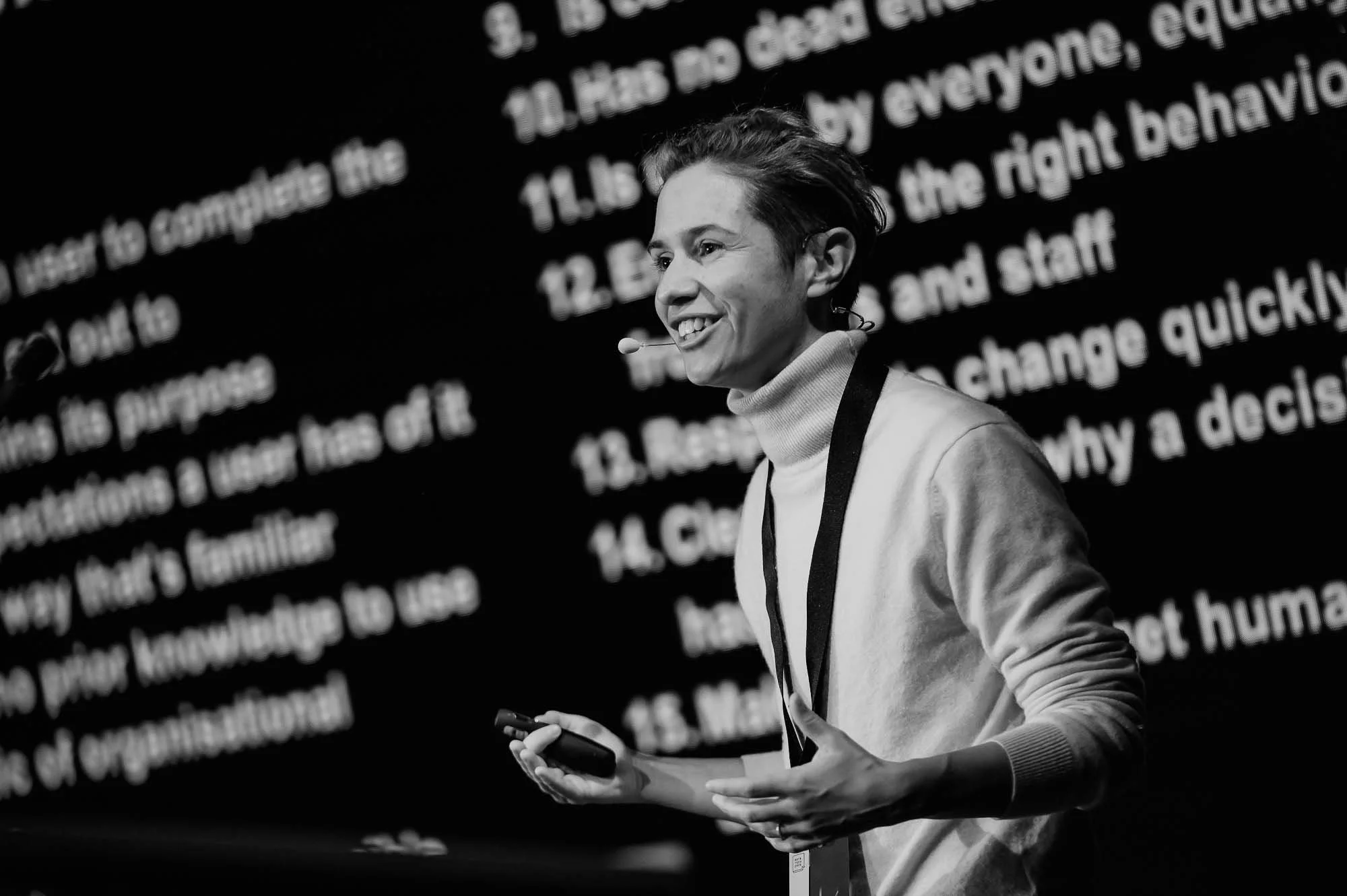 A person in a white poloneck stands in front of a screen giving a talk