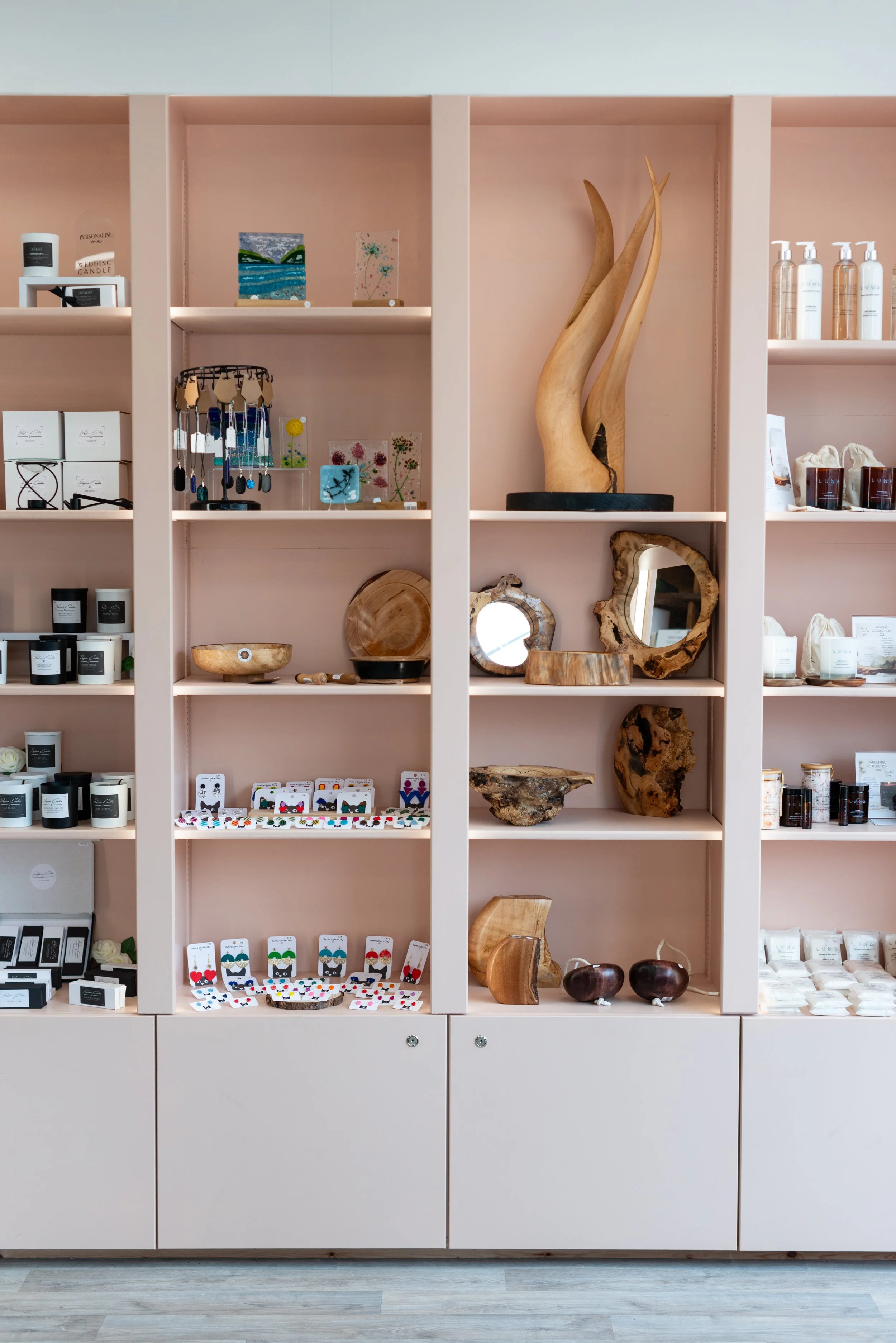 Display shelf with wooden sculptures, jewelry, candles, and decorative items in a store.