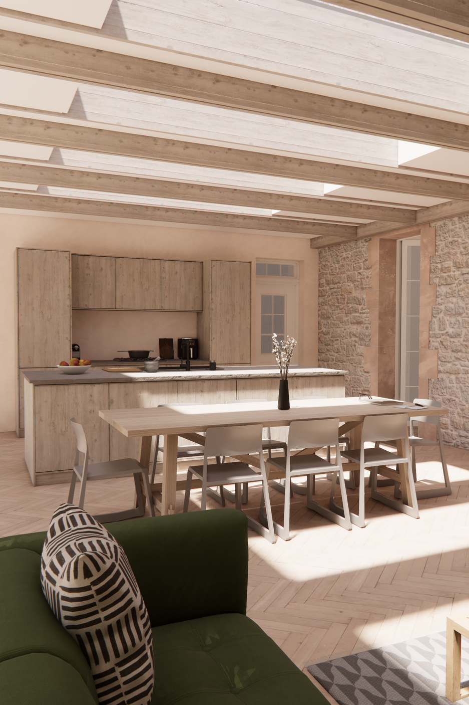 An open-concept kitchen and dining area featuring a wooden dining table with six white chairs, a kitchen with beige cabinets, a black vase with white flowers, a stone wall, and a green sofa with a black and white patterned pillow.