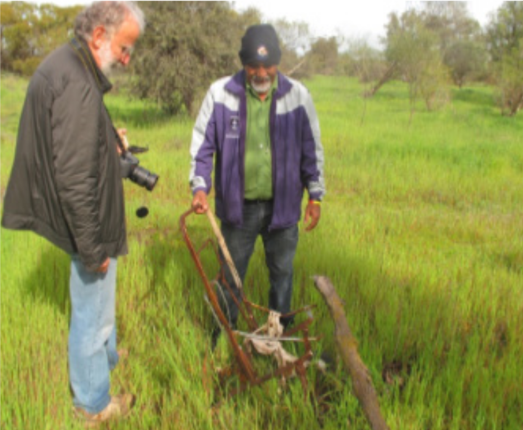 Thomas Cameron, the elected spokesperson for the Littlewell Working Group, talking with Community First Development volunteer Peter White. Both men are looking at an old pram on Littlewell Reserve and Thomas is explaining the significance of the old pram.