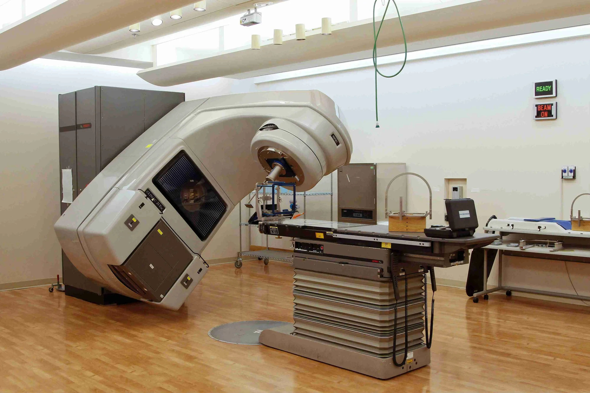 Radiotherapy machine in hospital room with wooden flooring and equipment.