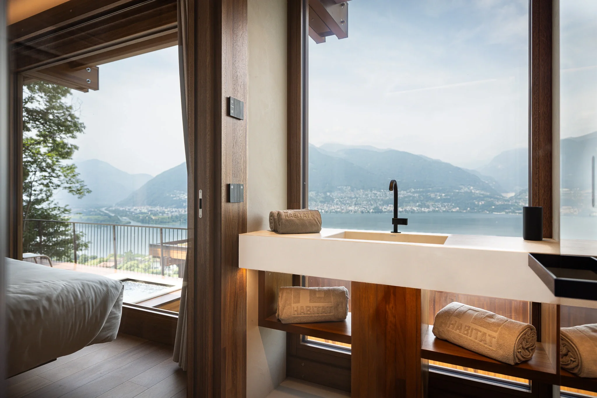Camera con vista lago e montagne, bagno con lavabo e asciugamani, arredamento in legno, letto visibile a sinistra.