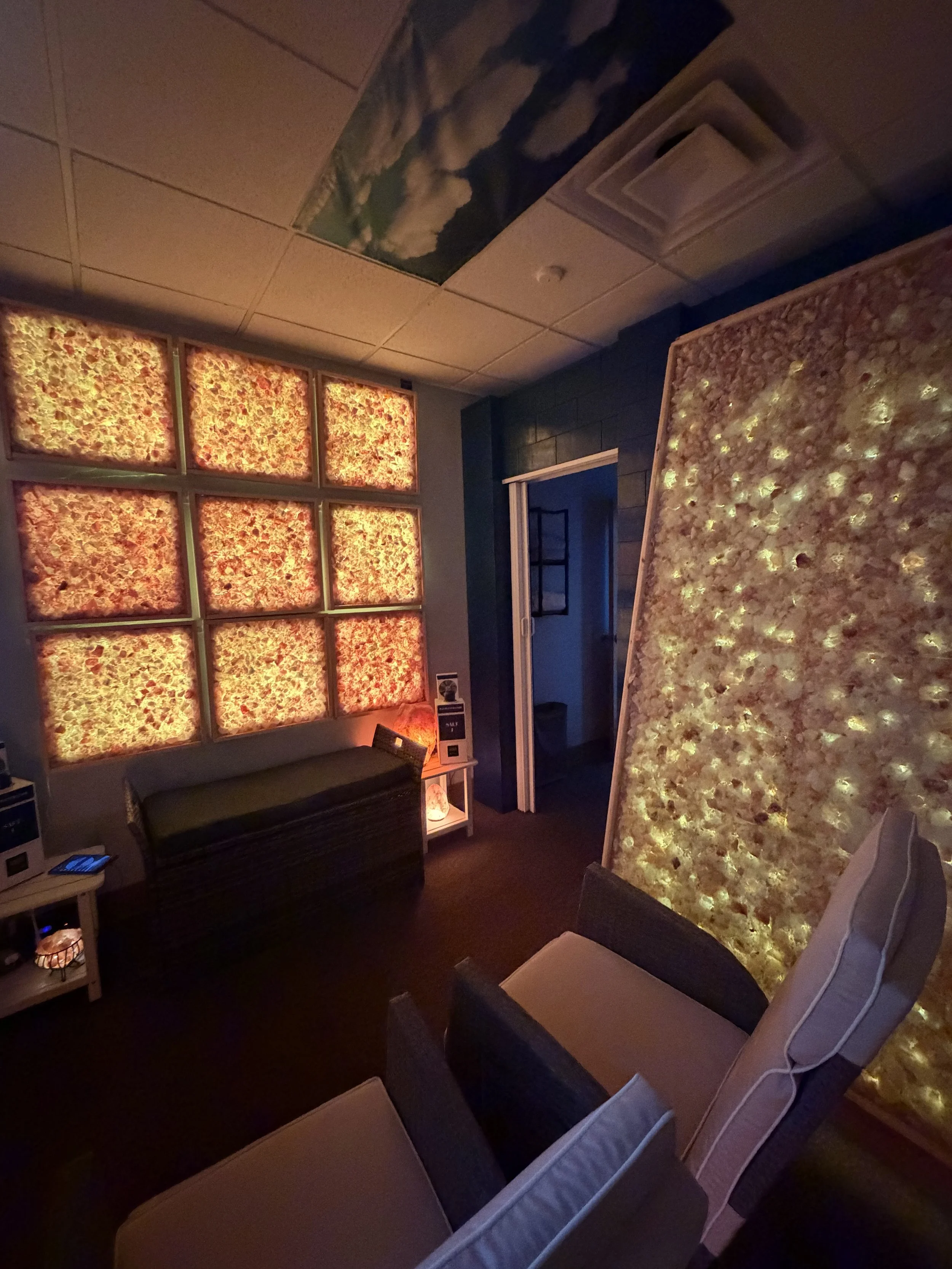 Warmly lit True Halotherapy salt room with illuminated salt walls and comfortable seating at Elite Retreat Wellness Center.