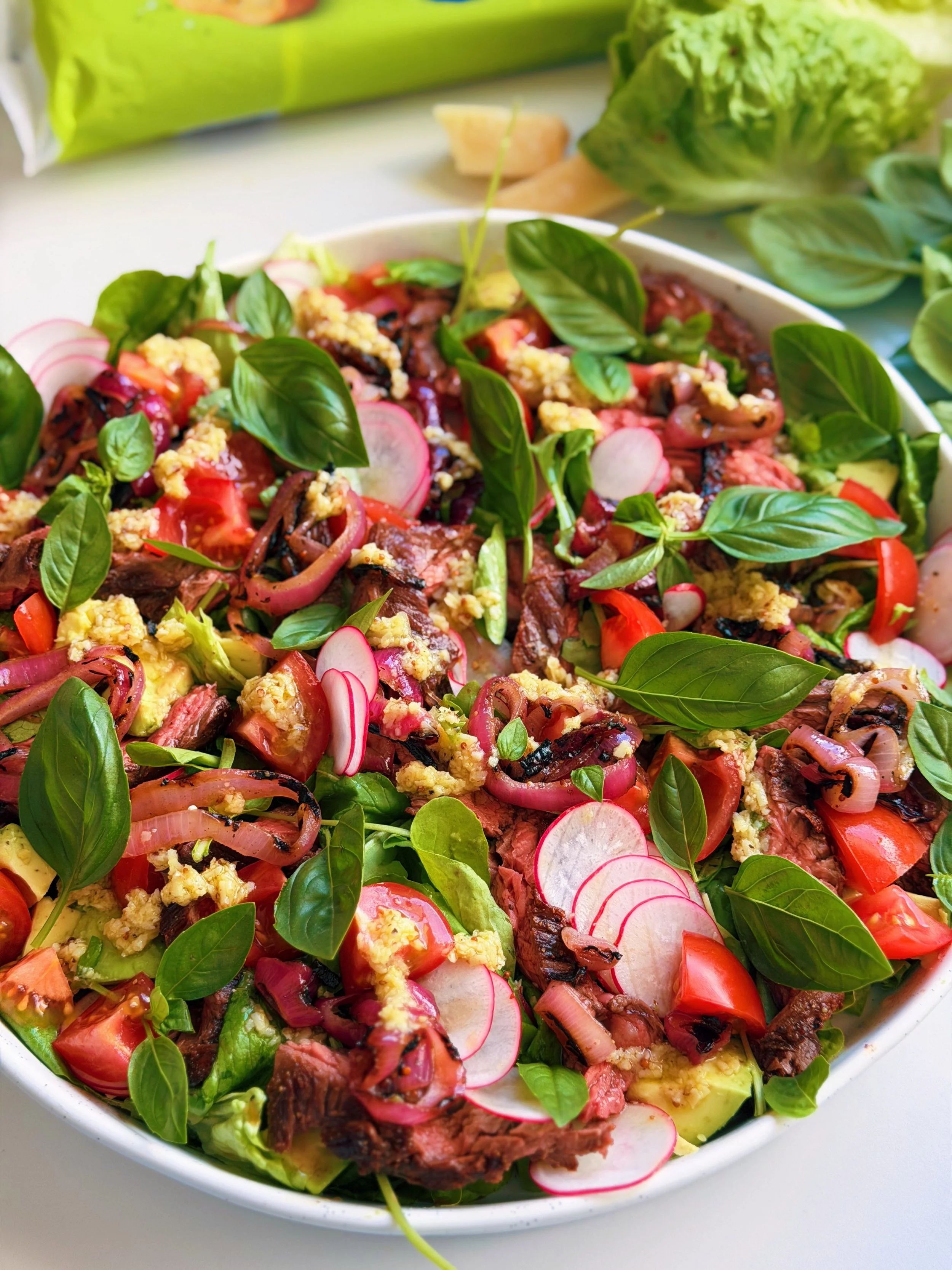 BBQ steak salad with sliced bavette steak, charred onions, avocado, tomatoes and Parmesan black pepper dressing.]