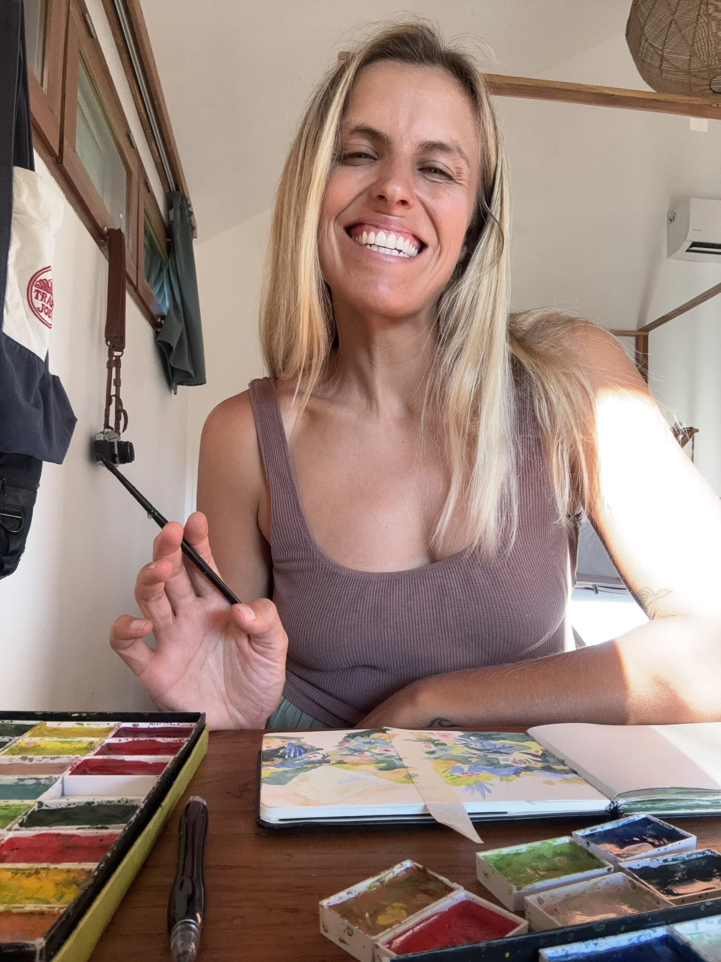 Photo of the artist behind Tropicool Studio holding a paint brush at her desk