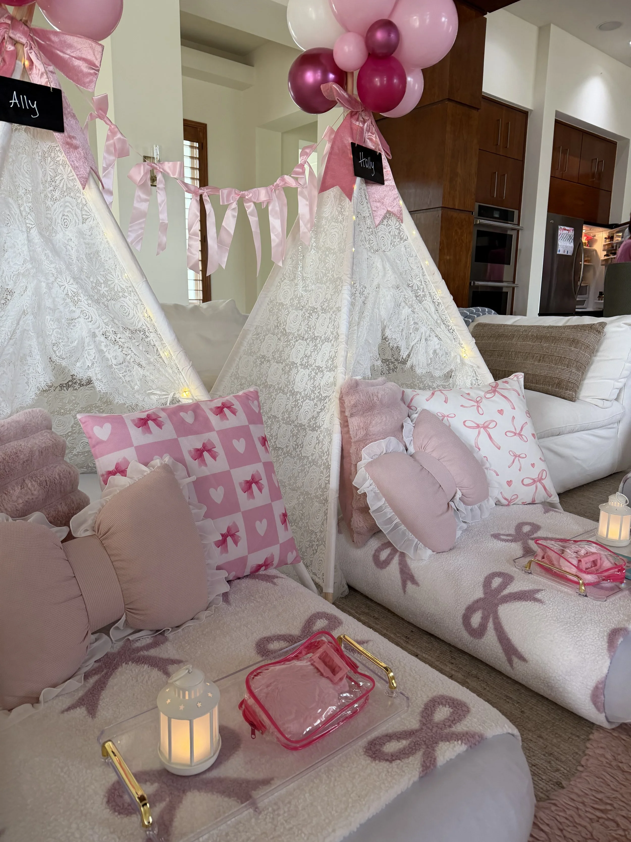Decorated indoor space with lace tents, pink and white pillows, balloons, a lantern, and a pink storage box, suggesting a celebration or girl's party.