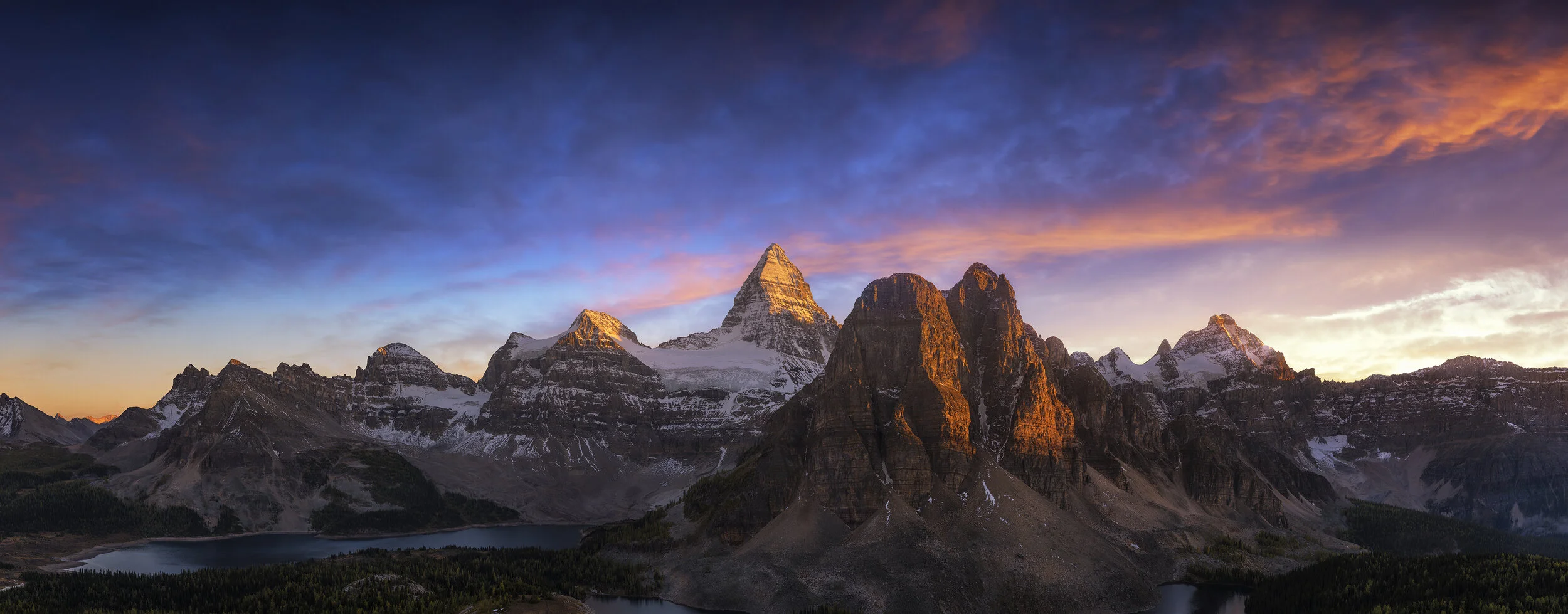 Sunrise over snow-capped mountains with clouds and a lake in the foreground.