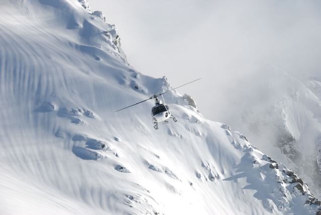Helicopter flying above snowy mountain slope.