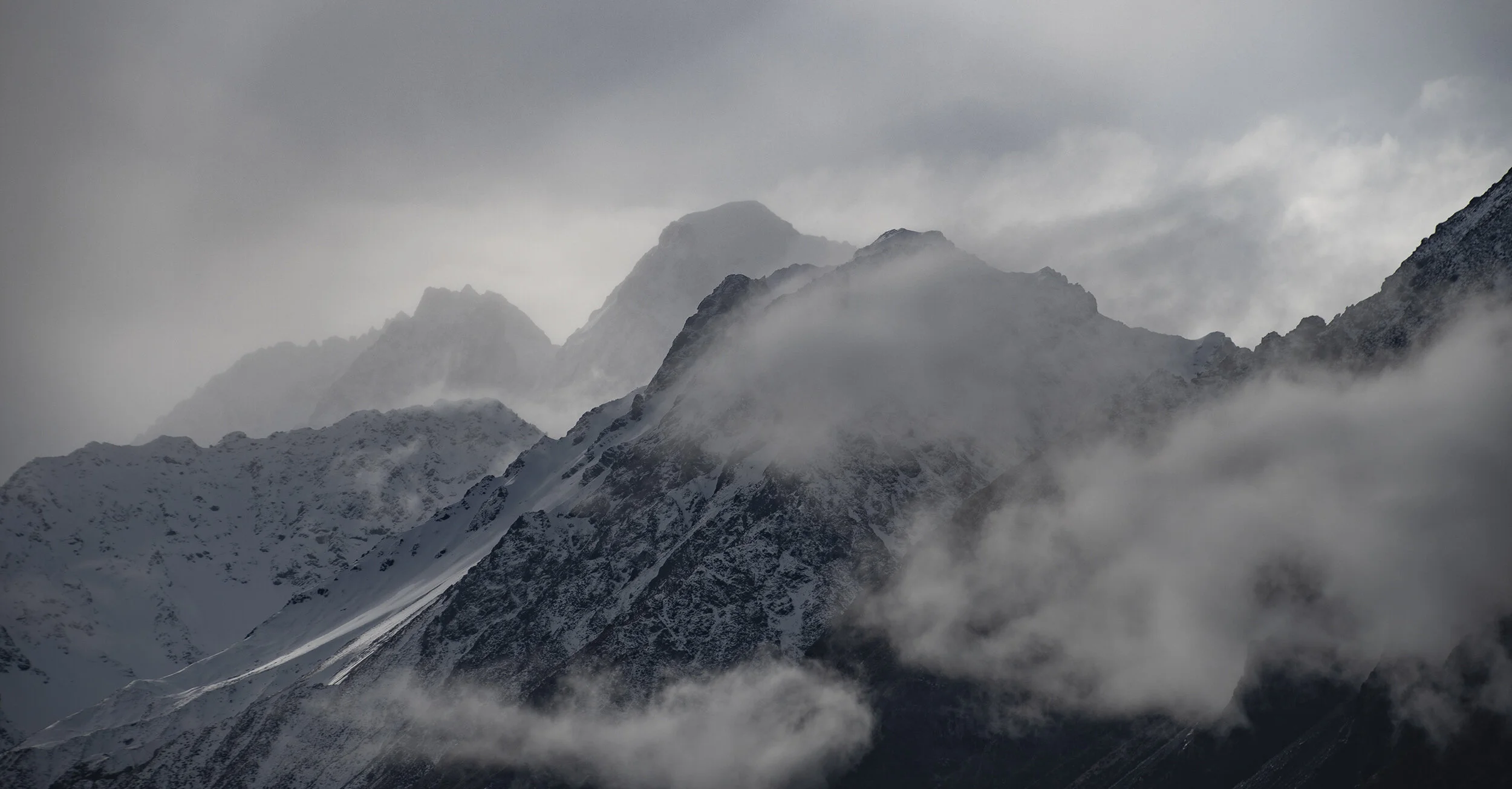 Snow-capped mountain peaks with clouds and fog in a mountainous landscape.