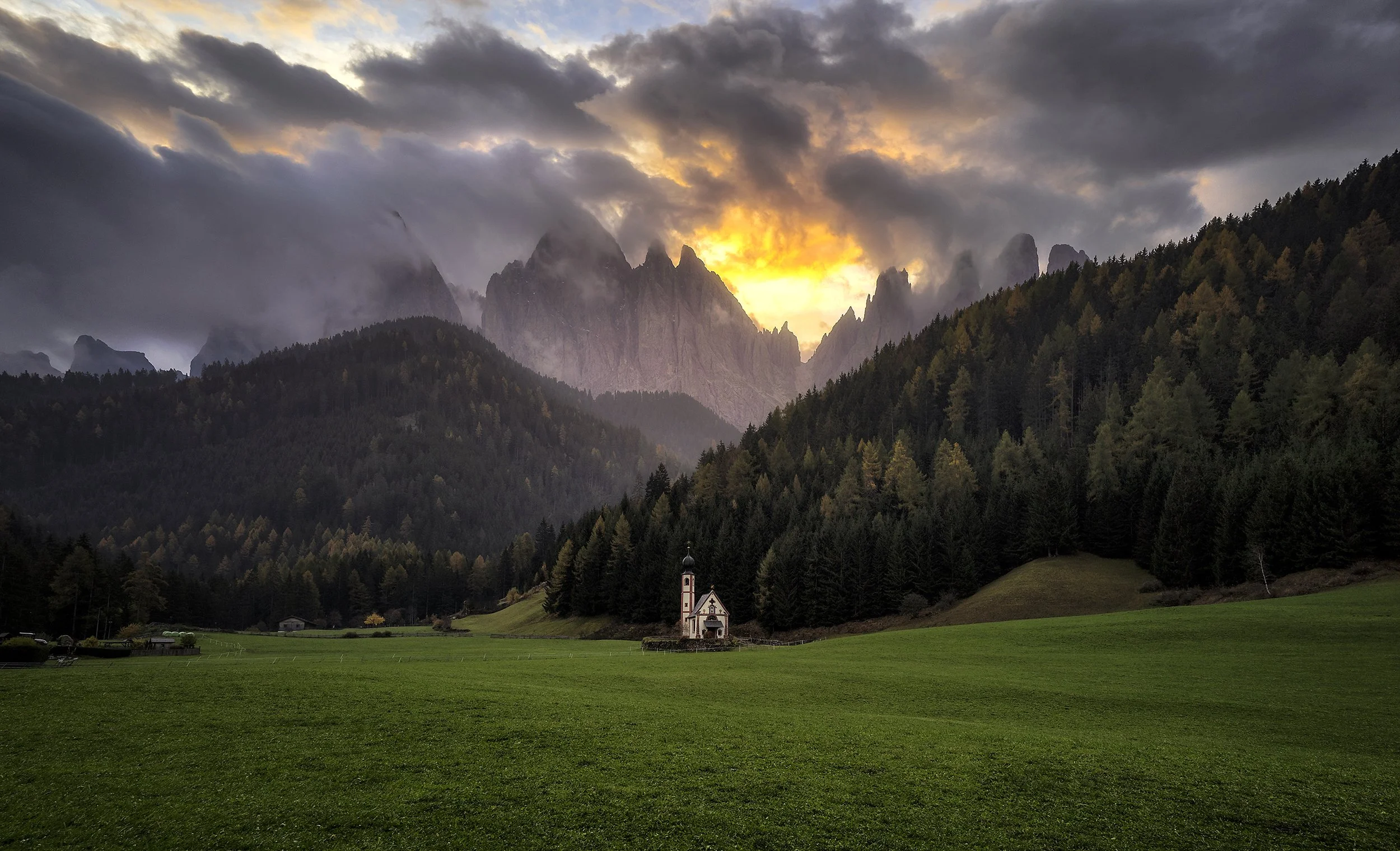 San Giovanni in Ranui church beneath dramatic storm clouds and the Odle mountains in Val di Funes, Dolomites, photographed by Timothy Poulton.