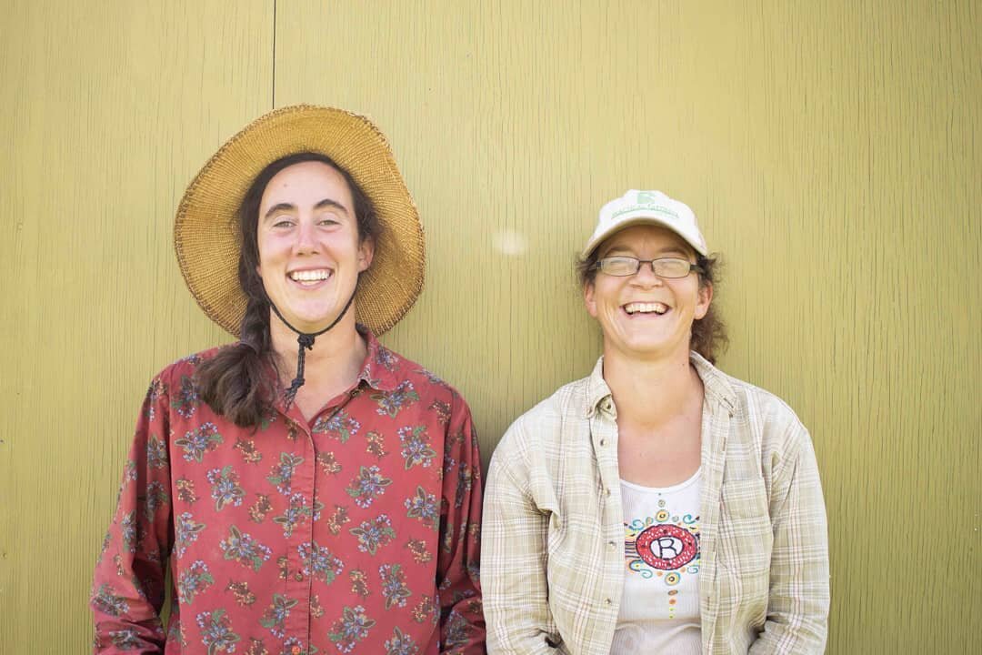 Two farmers smiling in front of yellow wall
